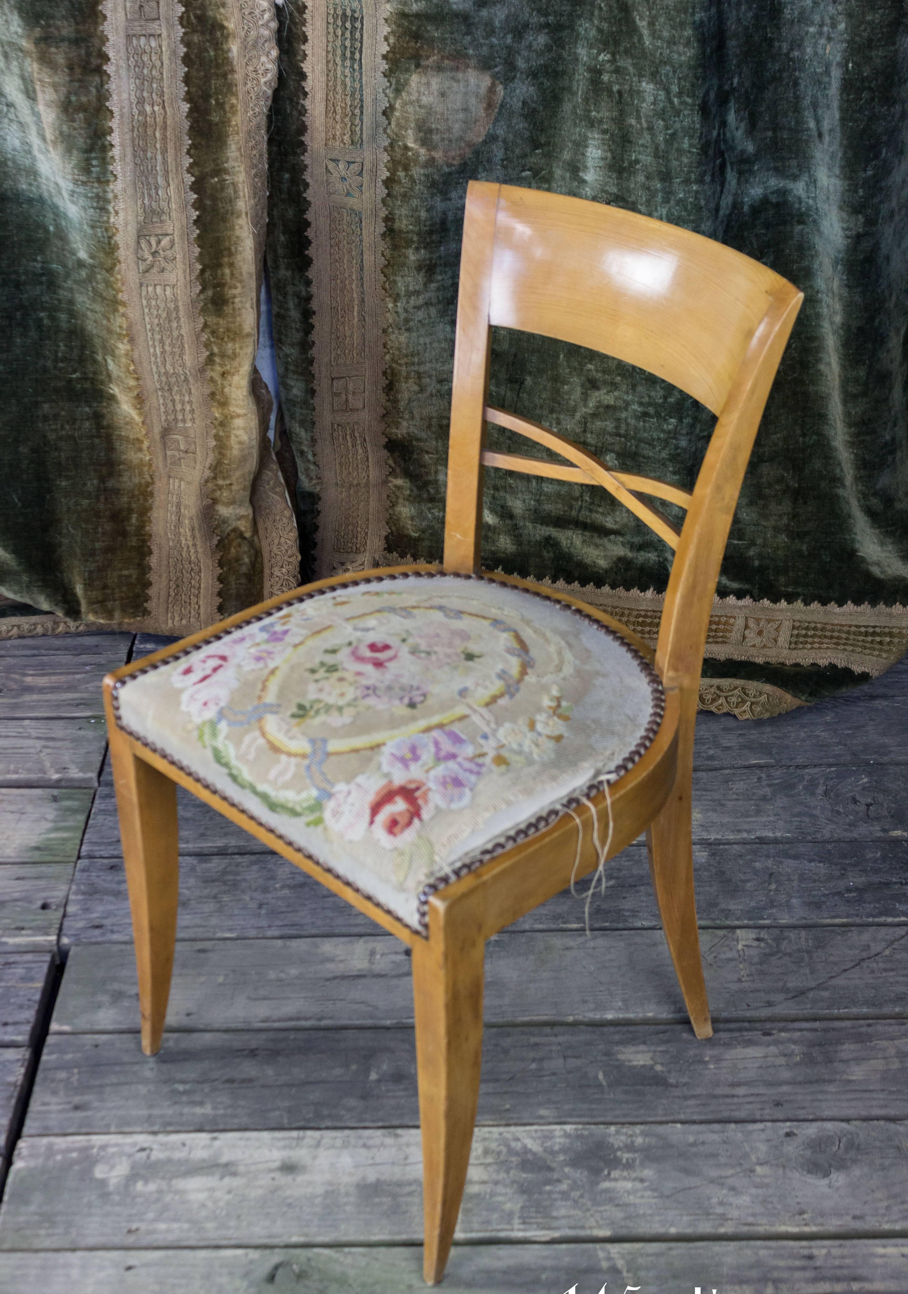 A classic pair of French 1940s side chairs with embroidered seats. This pair of French 1940s side chairs is an exquisite choice for any living space. The beautiful light wood frames and intricately embroidered seats are accented with brass nailhead