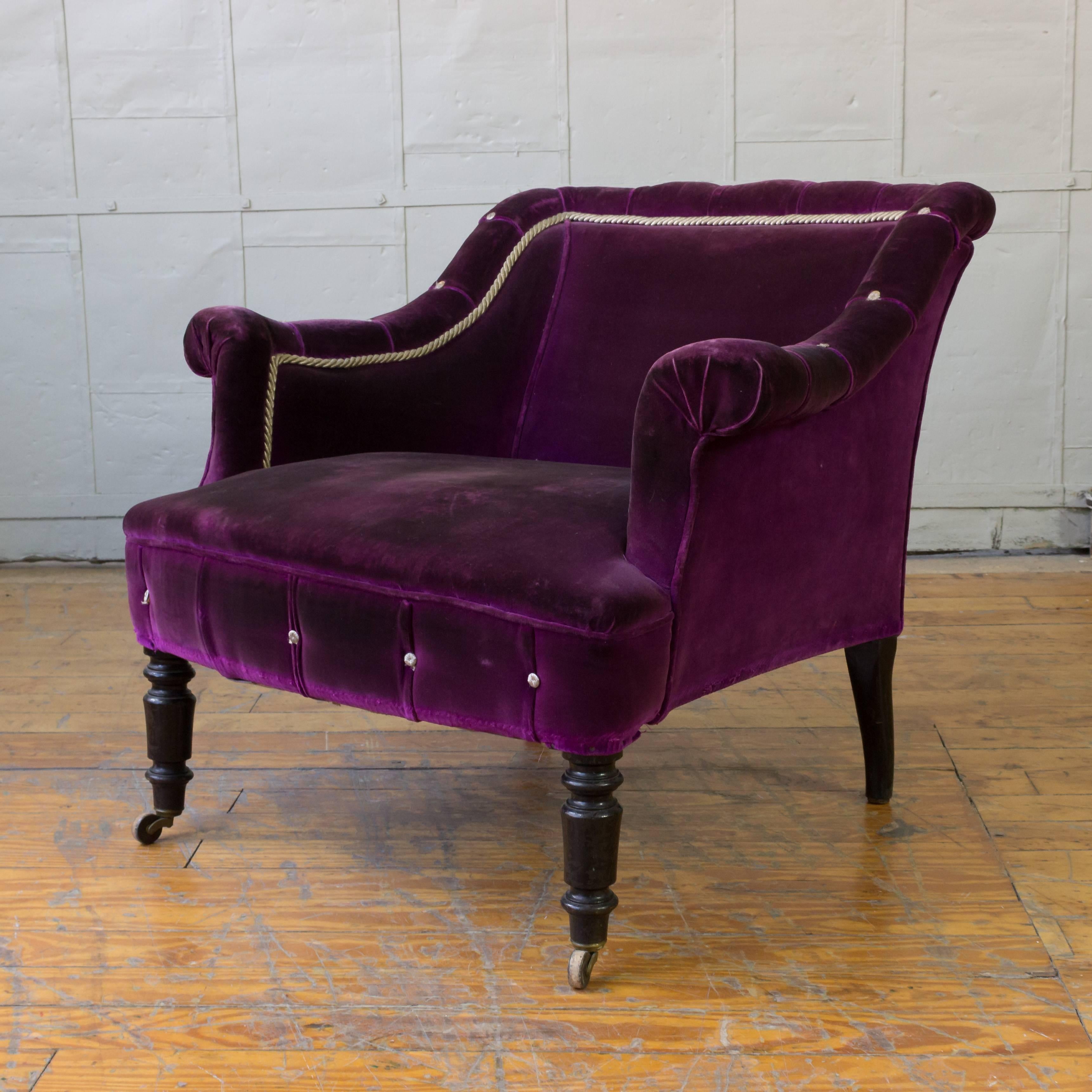 A captivating French 19th century distressed purple velvet armchair. Crafted in 19th century France, in the distinctive Napoleon III style, this armchair is elegant and timeless. It features low bankrolled arms, white braiding and buttons, and