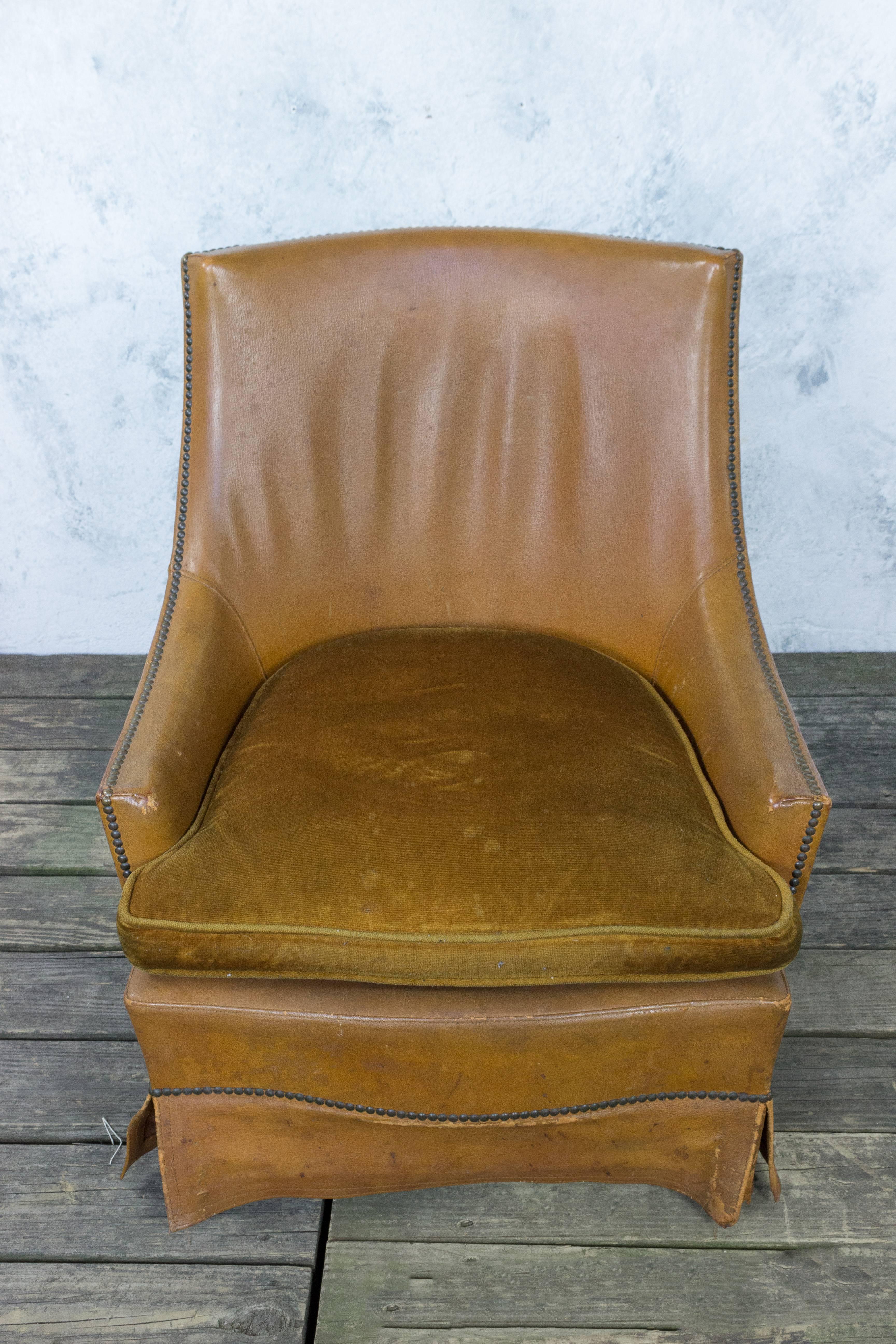 A striking French 1950s leather armchair with brass nailheads and leather skirting. Add a timeless piece of classic French style to your home with this 1950s leather armchair. Its brass nailheads and leather skirting give it an air of