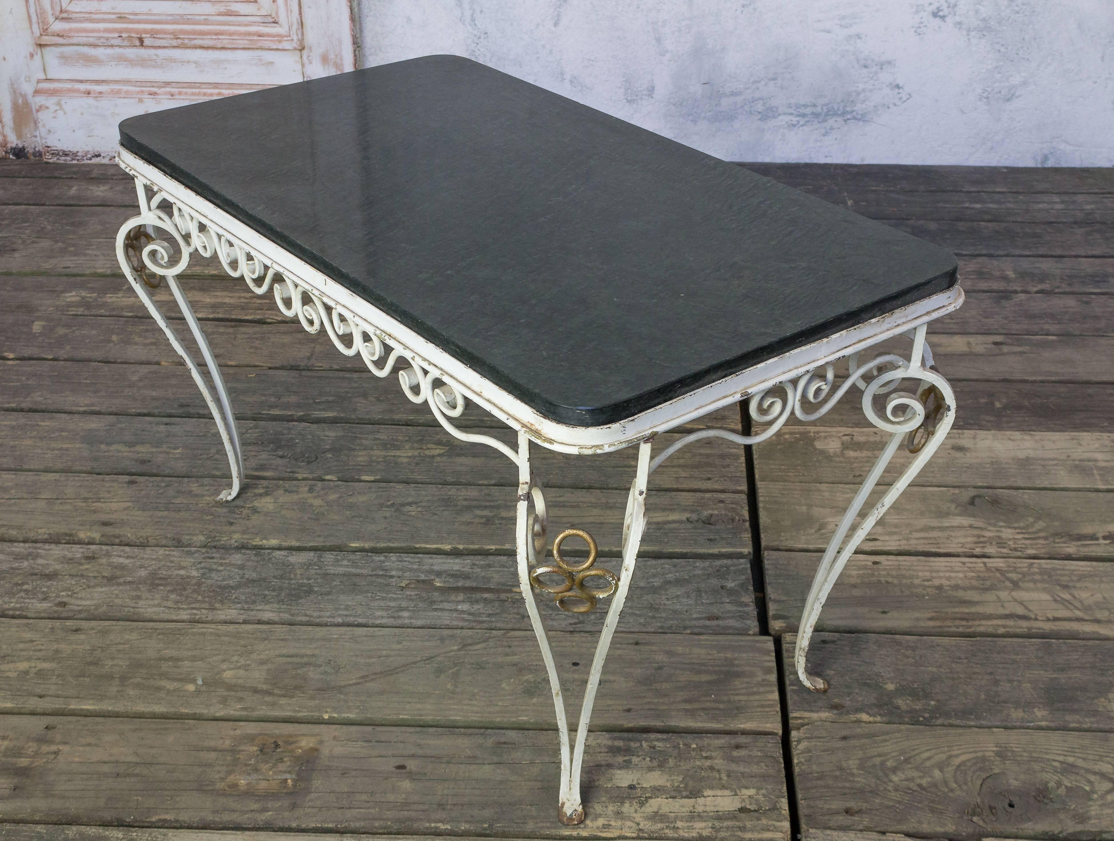 This French 1940s coffee table features a wrought iron frame with a black marble inset top, creating a classic and elegant look. The scrolled iron frame is painted in white with gilt accents, adding a touch of sophistication to the design.

In good
