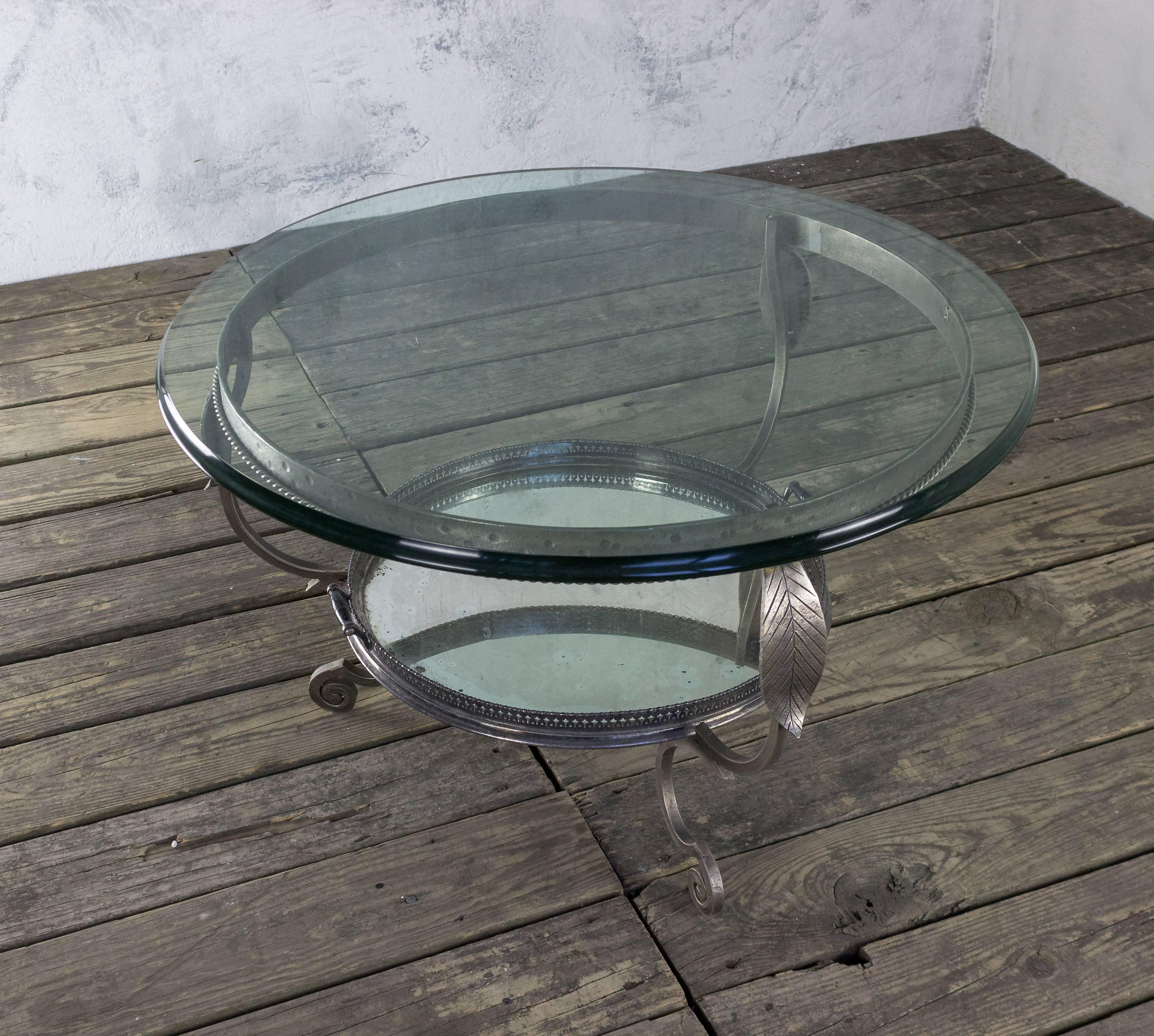 A stunning French coffee table from the 1940s, characterized by its stylish round design and a captivating glass top. This exquisite piece features a silvered metal serving tray elegantly resting on a shelf beneath the glass surface. Recently plated