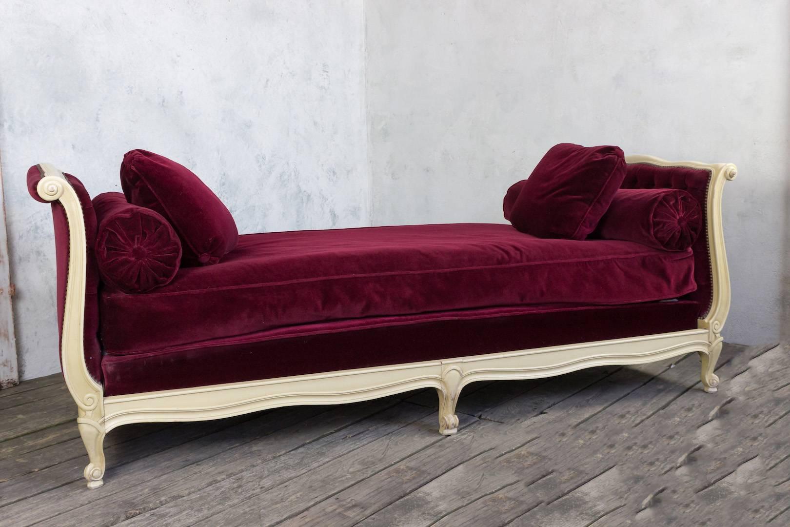 Sehr große und breite Liege aus Frankreich, um 1940, mit cremeweiß patinierter Oberfläche. Das Bett ist mit einem luxuriösen bordeauxfarbenen Samt bezogen, Kopf- und Fußteil sind getuftet. Die Liege ist in sehr gutem Zustand.