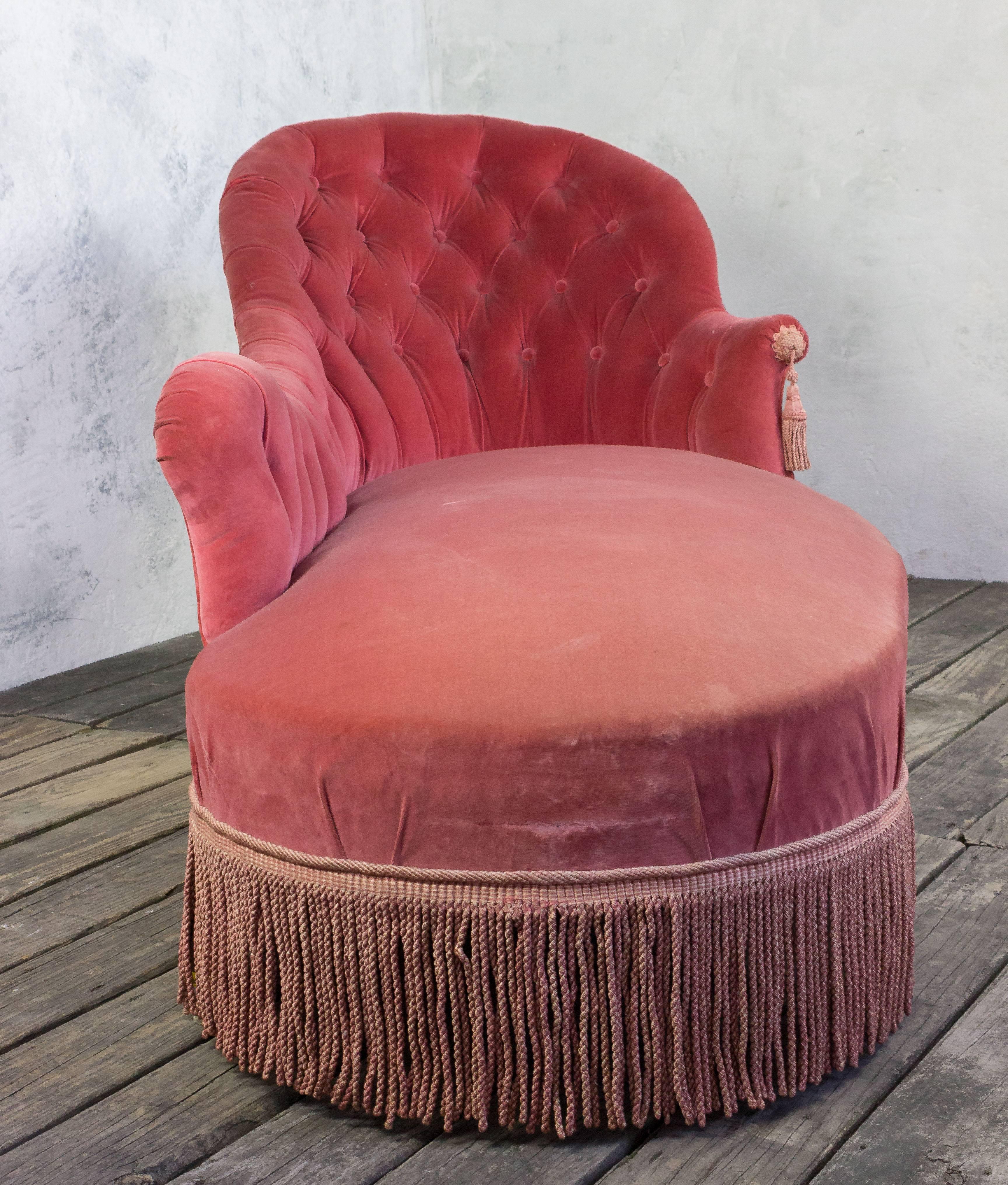 An asymmetrical (right arm) tufted French chaise longue, upholstered in salmon colored velvet with matching bullion fringe. 

.