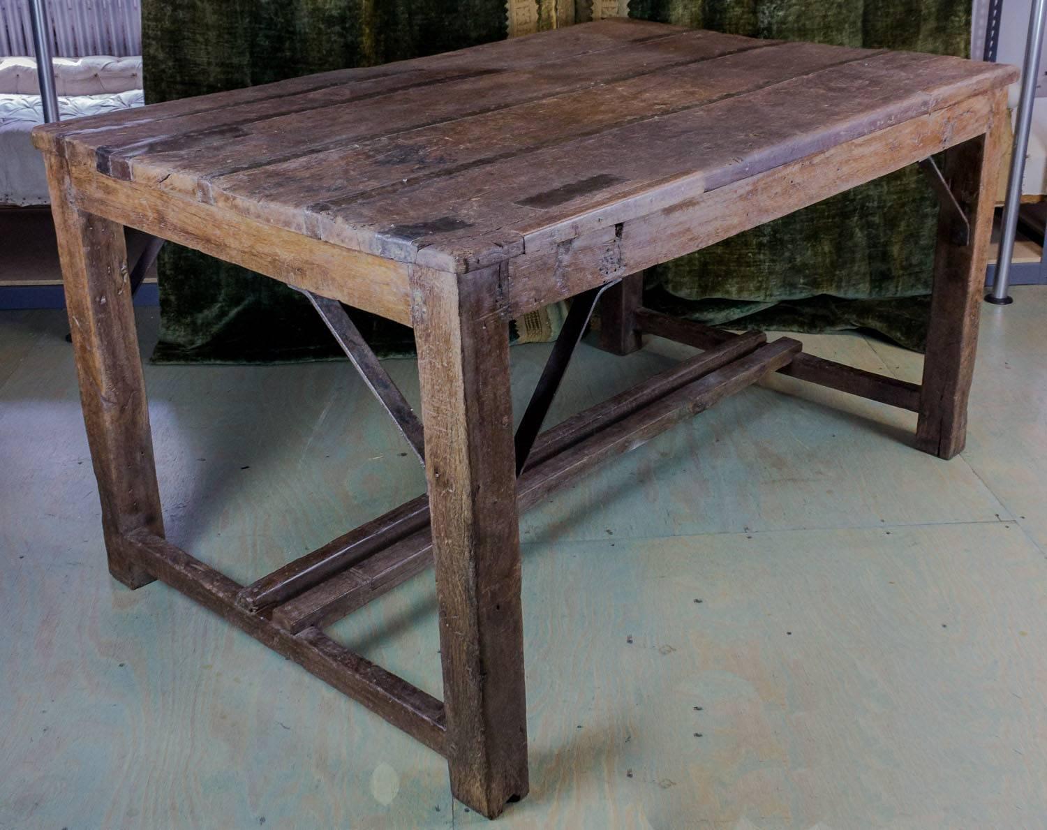 Large rectangular wood work table with iron straps connecting the boards and iron supporting brackets.
