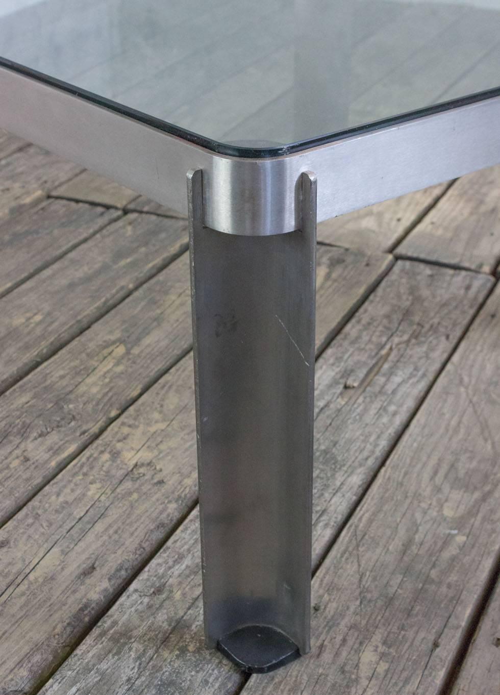 This vintage coffee table, originating from France in the 1980s, features a brushed aluminum and glass construction that embodies the classic design of the era. The table's square shape is softened by rounded edges, creating a harmonious blend of