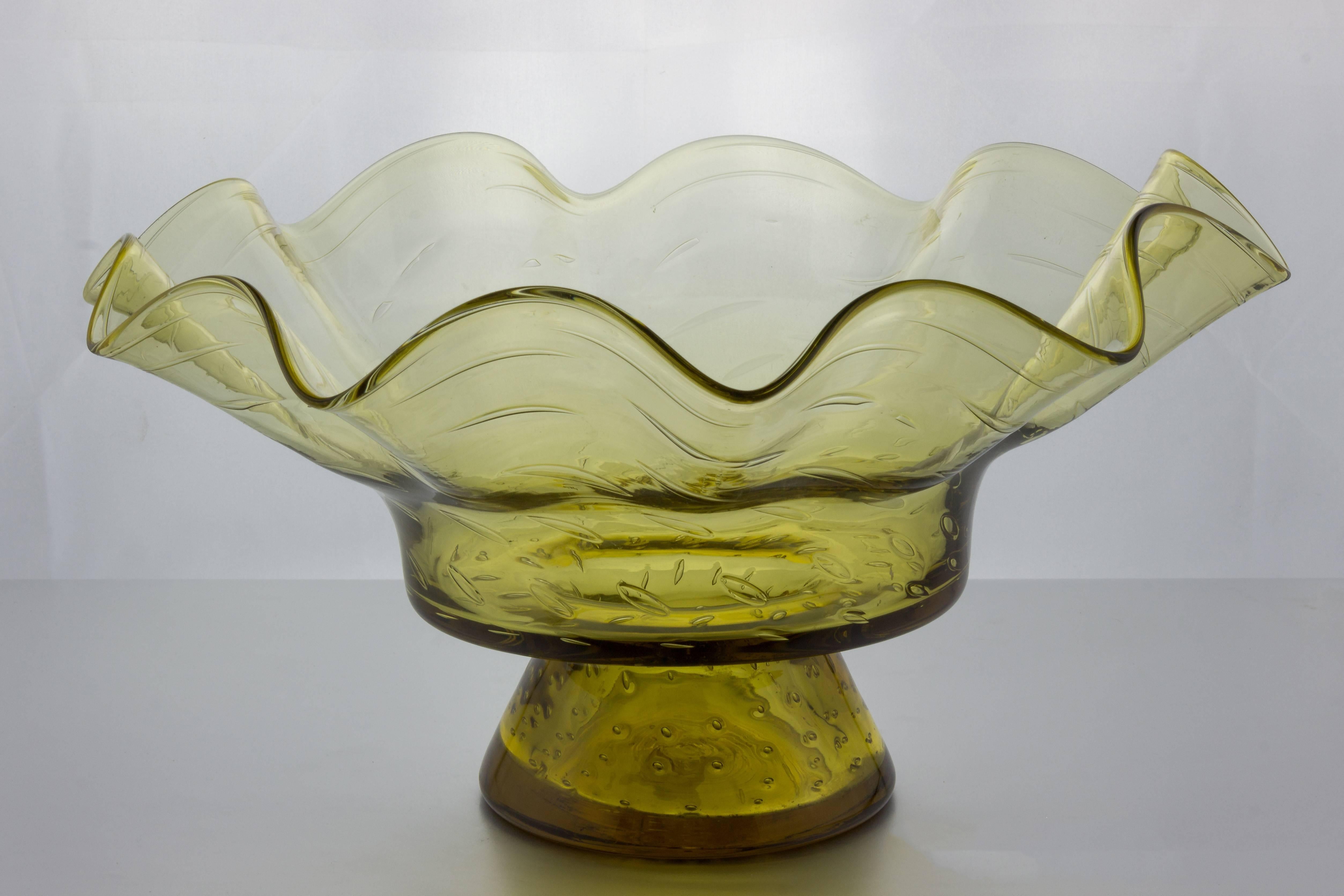 This  American 1960s Blenko glass bowl  is a charming embodiment of vintage beauty. Its ruffled design and light yellow color create a delightful visual appeal, while the bubble inclusions in the glass add a unique touch of character. The bowl