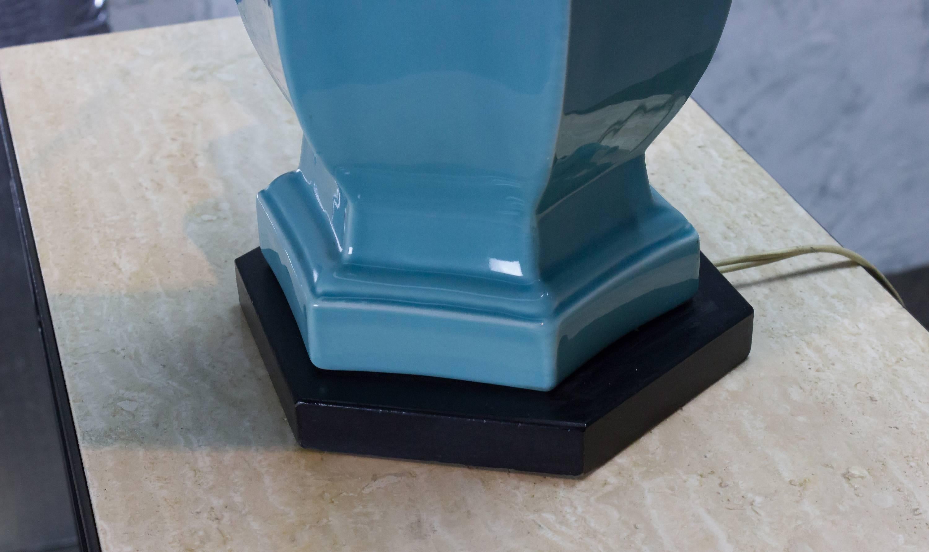 This 1950s American glazed ceramic lamp has a unique design that features a beautifully detailed ceramic body, finished with a high-gloss glaze in turquoise blue. The lamp sits atop a sleek black wooden base that perfectly complements the ceramic