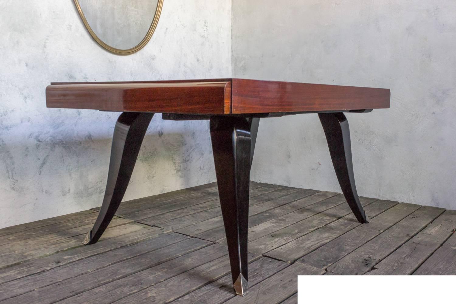 This captivating French 1940s Art Deco rosewood veneered dining table features gracefully curved ebonized legs with nickle plated sabots. The table has two 15 inch leaves that fit in on either end, making it incredibly versatile. In good vintage