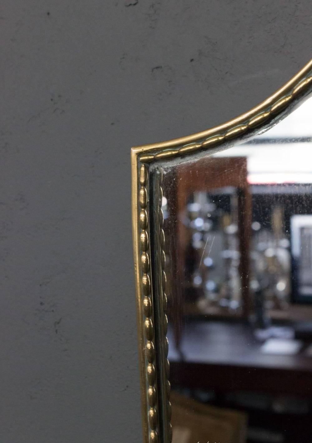 Beautiful shield shaped mirror, Italian, circa 1950. The brass frame has a beaded design.