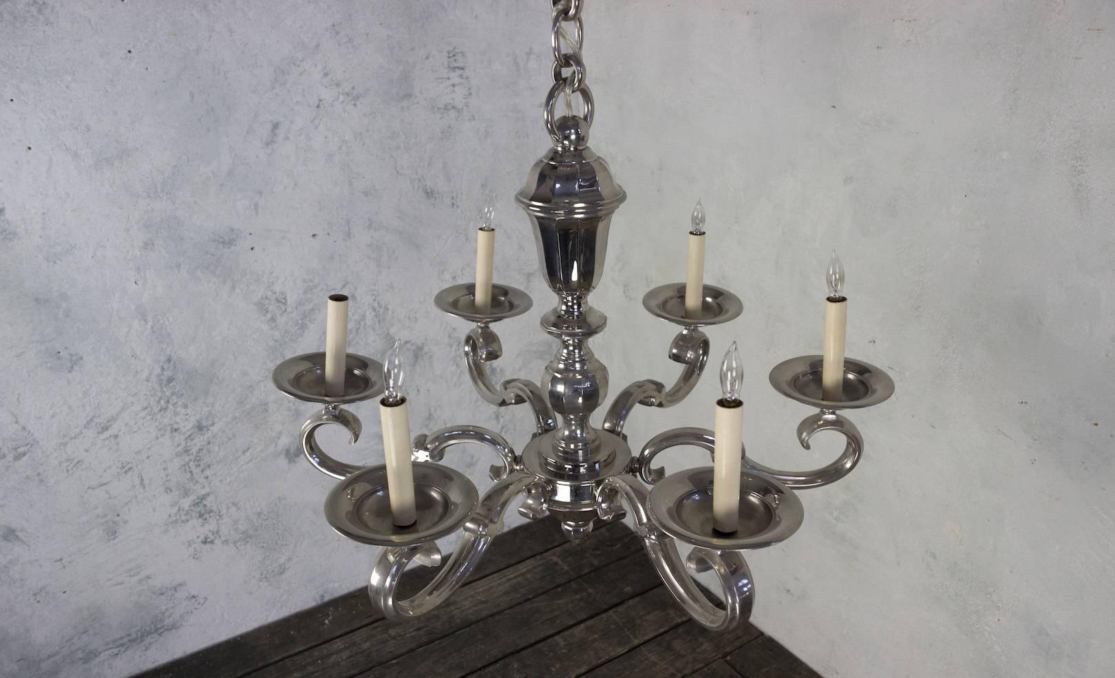 This elegant French 1940s nickel plated bronze six armed chandelier emanates an aura of sophistication and grace. This timeless piece includes a matching chain and canopy, adding to its overall allure. Recently rewired, it ensures optimal