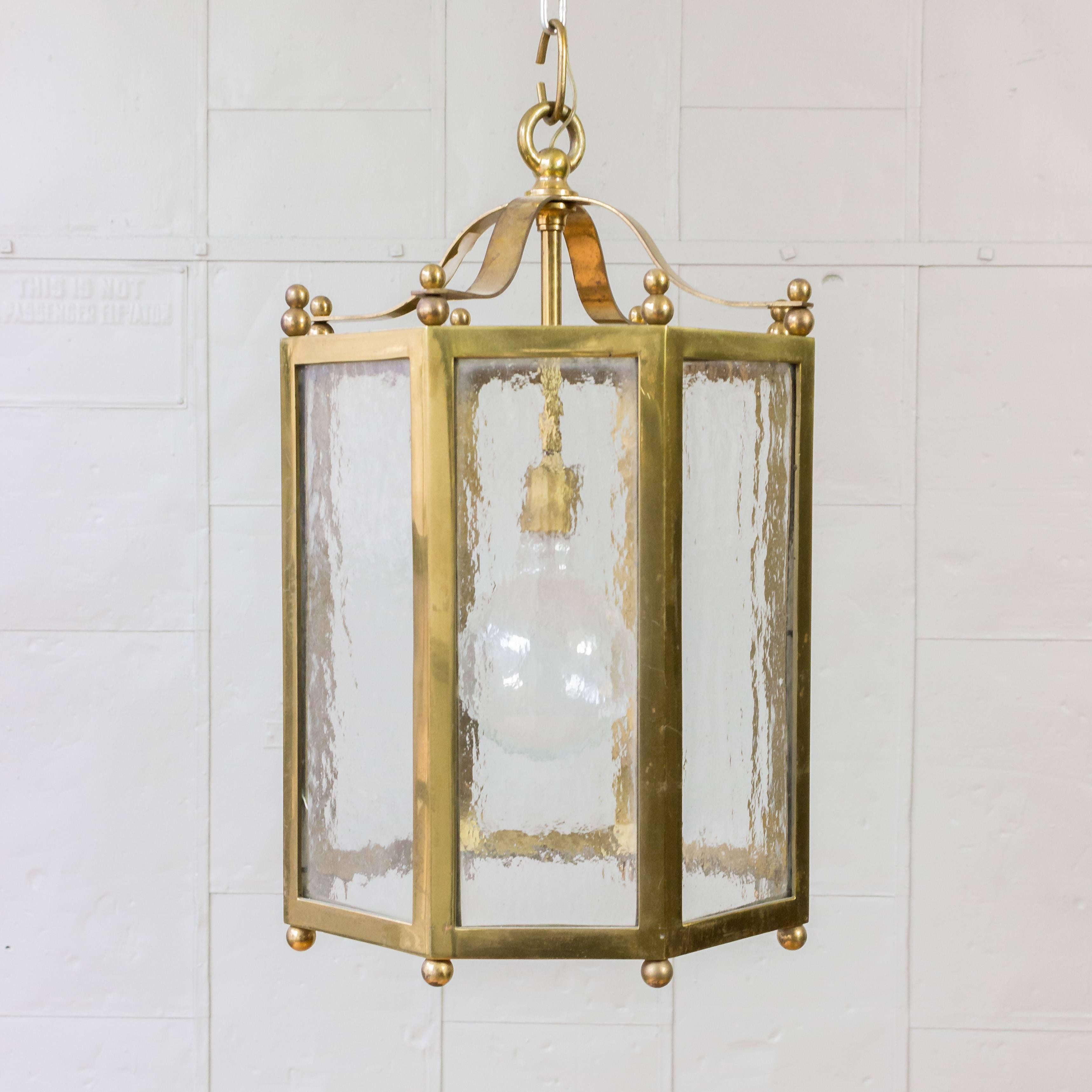 An elegant  French brass and glass octagonal lantern composed of eight intricately-textured glass panes encased within a sleek brass frame. This stunning lantern emits a warm and welcoming glow that adds charm to any indoor or outdoor space.