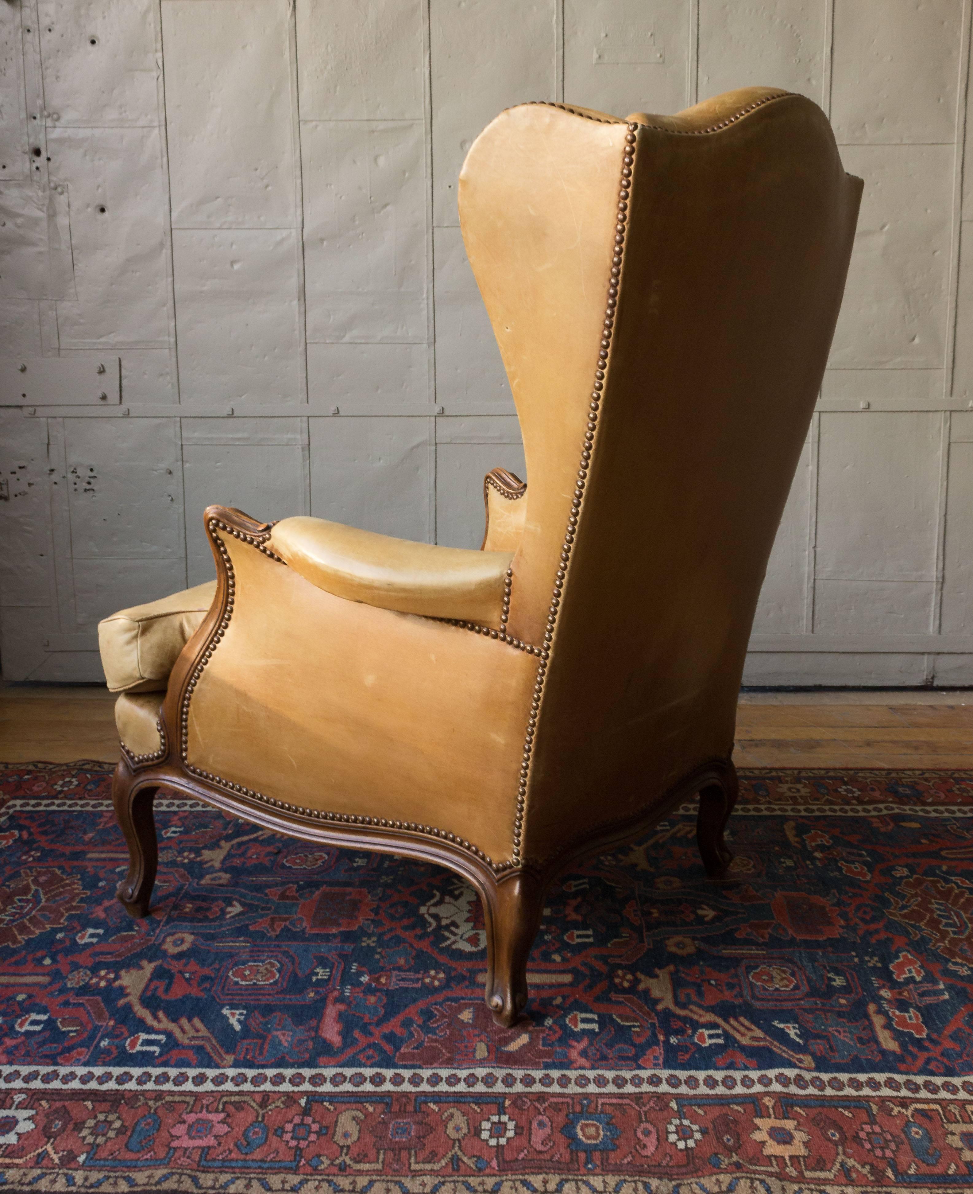 A very comfortable Louis XV style wingback armchair upholstered in a soft tan leather. Add a touch of old-world sophistication to your living space with this exquisite American Louis XV style wingback armchair. Upholstered in a soft tan leather and
