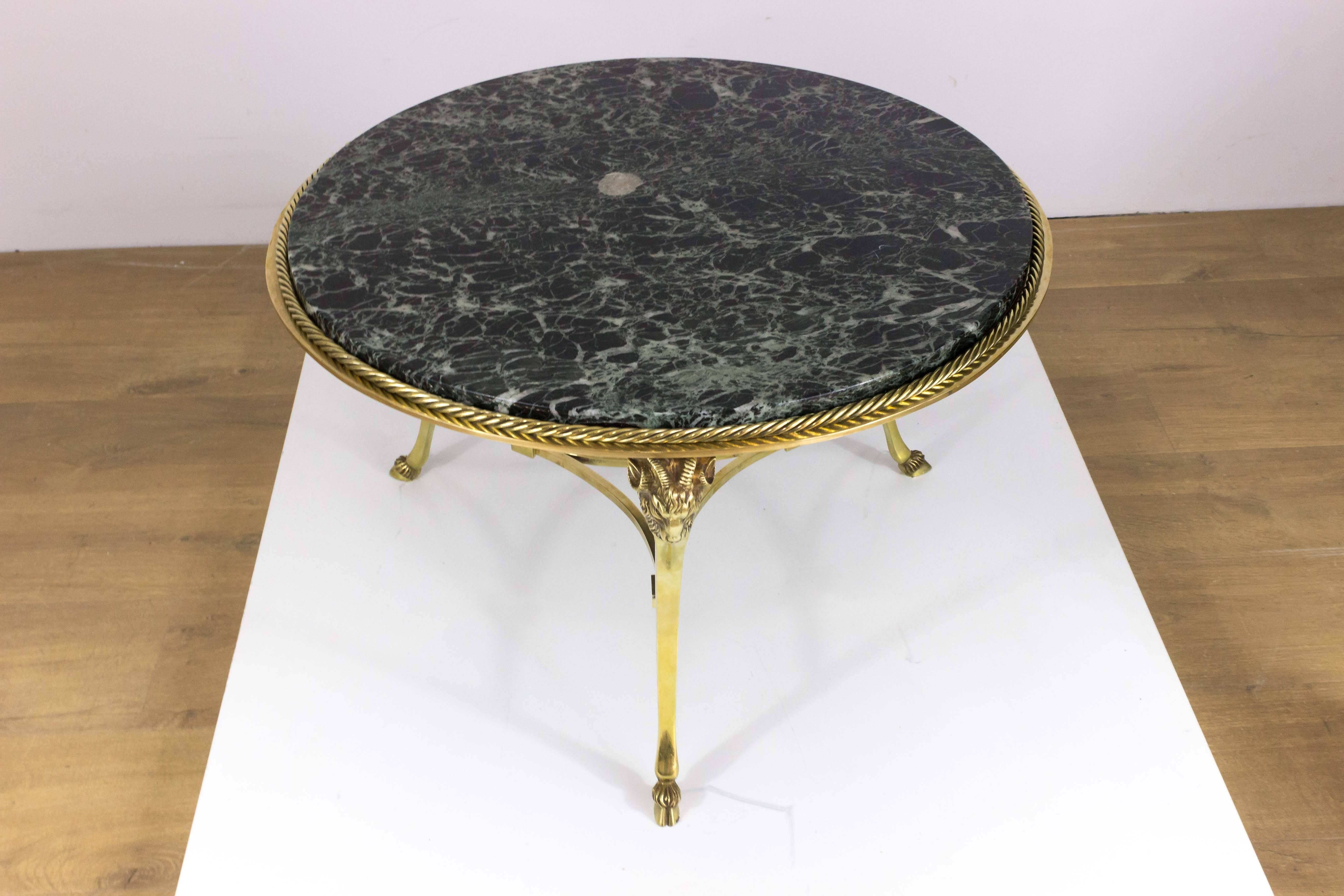 French 1950s brass and bronze coffee table with veined marble top resting on three legs. The top has a twisted roping detail and each leg has a ram's head on the top of the legs and hoofs at the base. 

This piece is still in France, please