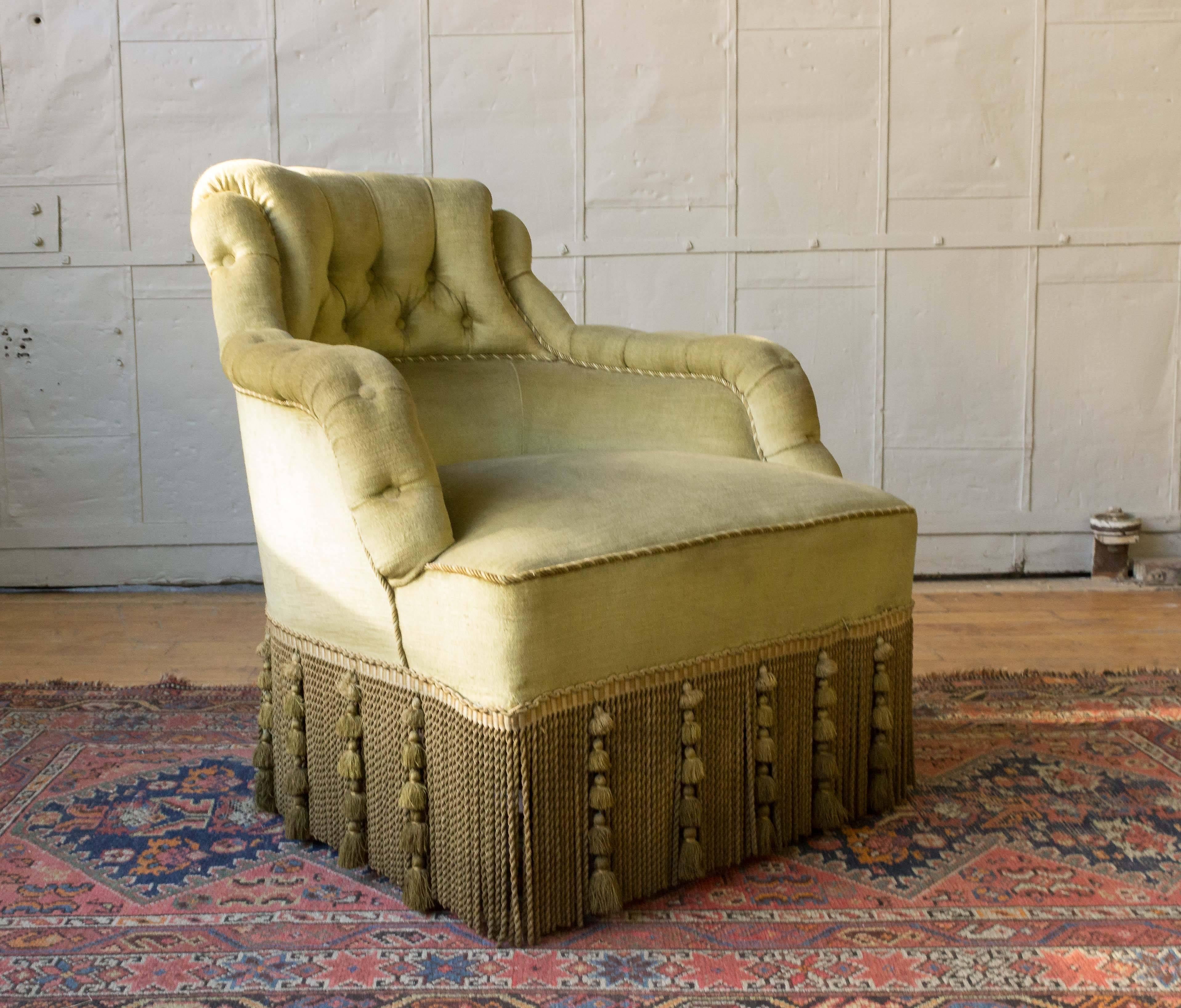 An exceptional French 19th century Napoleon III reading chair. This unique chair is upholstered in an elegant green-gold velvet, featuring intricate braided detailing, and elaborate decorative fringe that create a timeless, sophisticated look. The