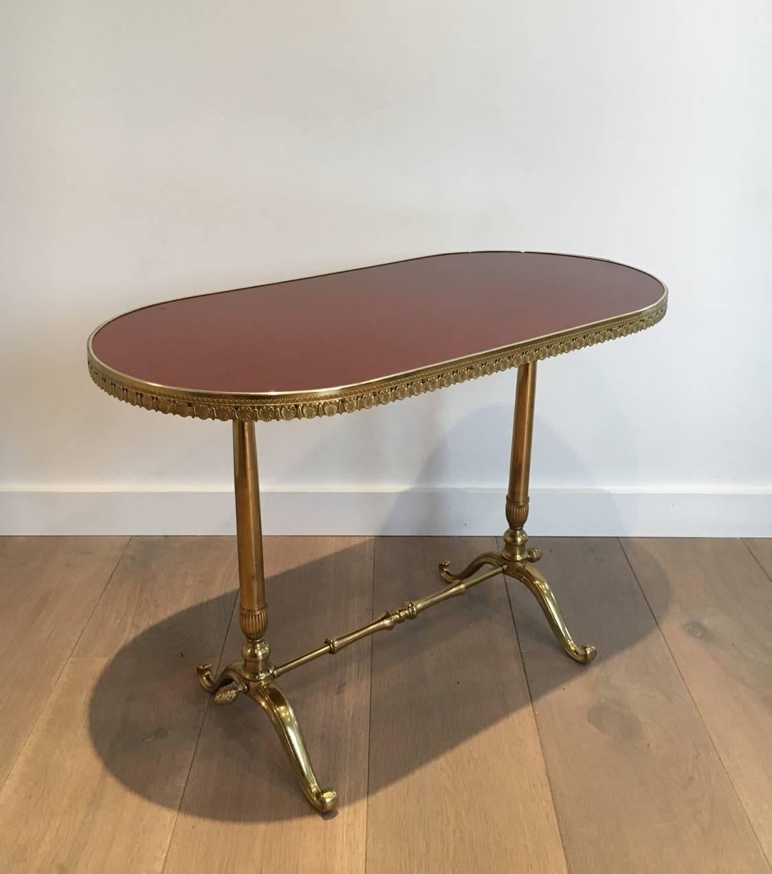 A handsome neoclassical style oval side table, having a brass and bronze base and a lacquered wooden top. The top is finished with a brass gallery decorated with classical Greek motifs. The base has curled feet joined by a turned stretcher and