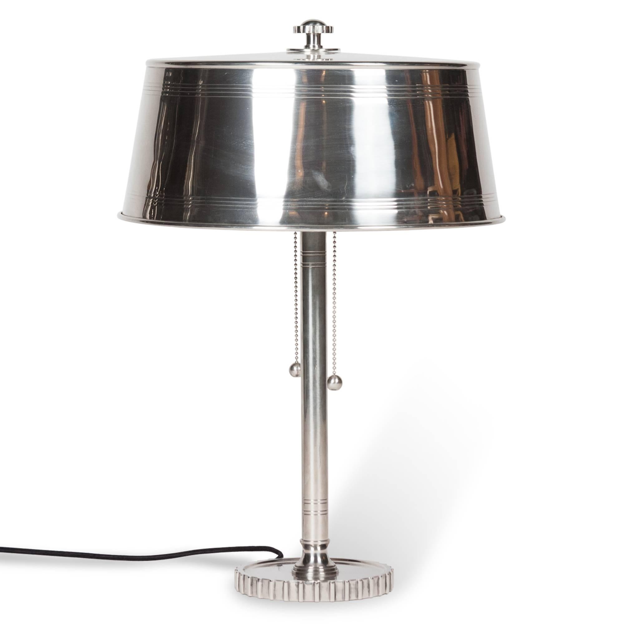 Nickel table lamp, the circular base in the shape of a gear, of column-form with nickel shade, gear-top finial, two ball chain pulls by Walter Kantack, American, late 1920s. Measures: 21 ¼ in. overall height with finial, 14 ½ in. diameter (shade). A