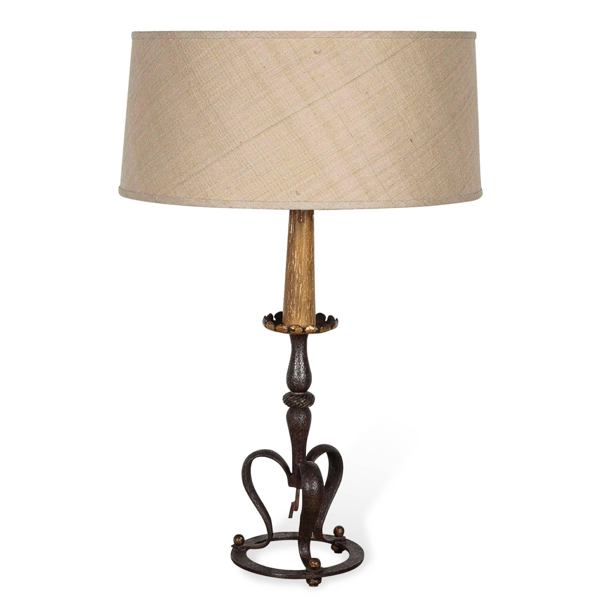 A wrought iron and gilt table lamp, candle style with three leg base, by Gilbert Poillerat, French, late 1930s. In custom shade. Measures: Diameter of base is 6 3/8 inches. Overall height 24 in. Diameter of shade 16 in.
    