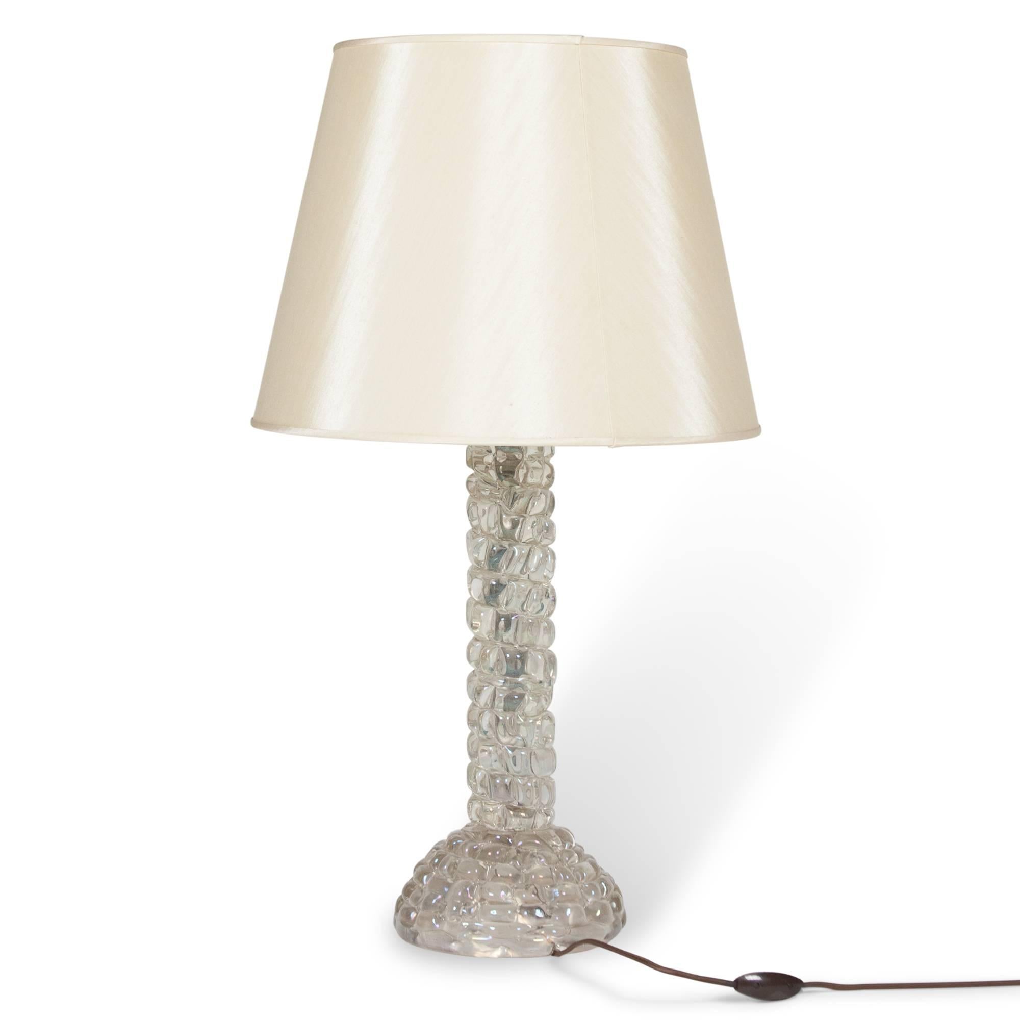 Glass table lamp, clear glass with gold inclusions, of simple column-form with rounded base and textured on the surface with raised squares, by Barovier e Toso, Italian, 1940s. In a custom satin silk shade. Measures: 8 in. D base, 15.5 in. D shade