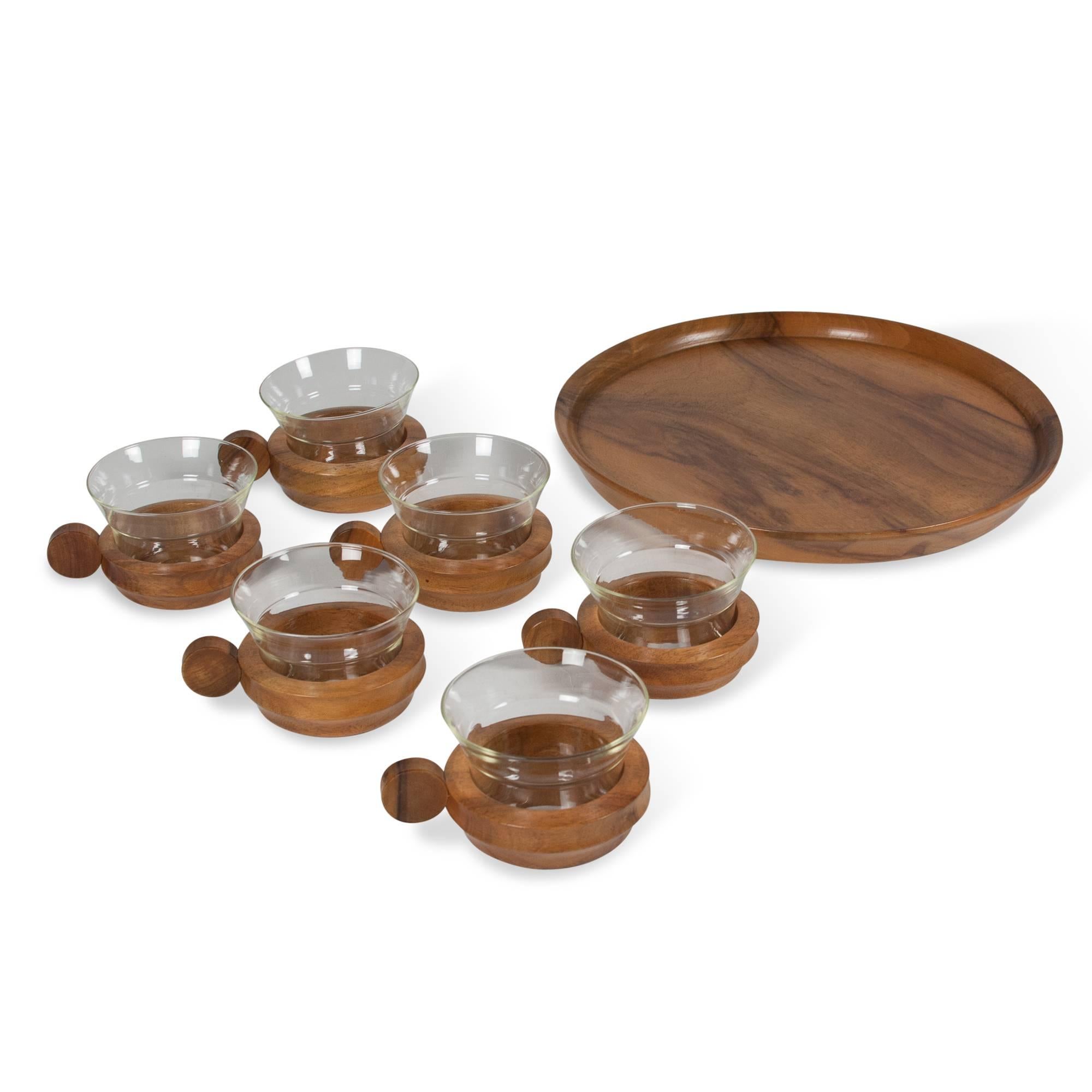 Walnut and glass drinking set comprised of six glasses with handled holders and a round serving tray, Austria, 1960s. Measures: 11” D, 3” H. 