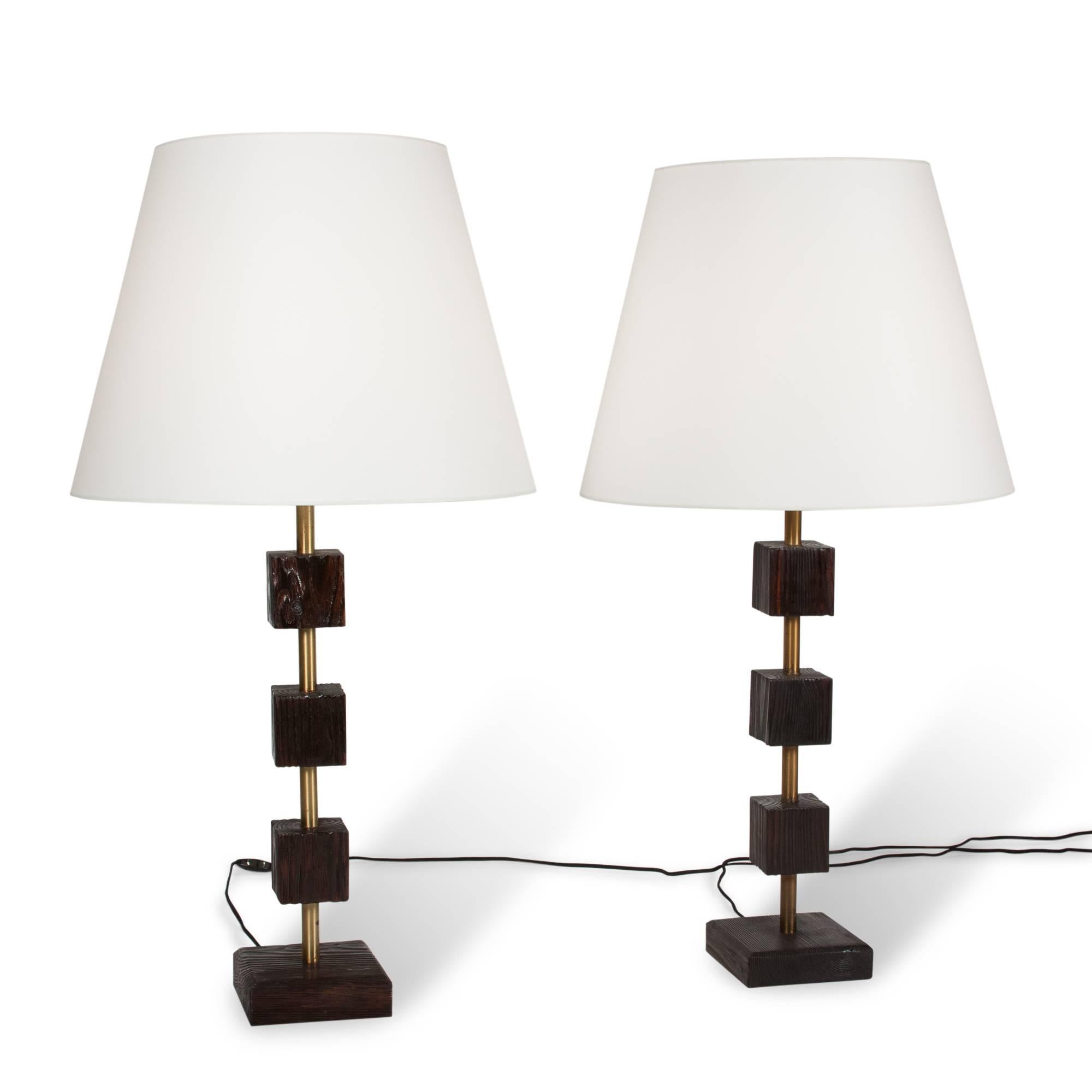 Pair of table lamps in ebonized pine and brass, pine cubes stacked and spaced along length of the brass rod, American, 1950s. In custom shades. Measures: 6 in.sq. base, 36 in. H, 19 ¼ in. D shade at widest.