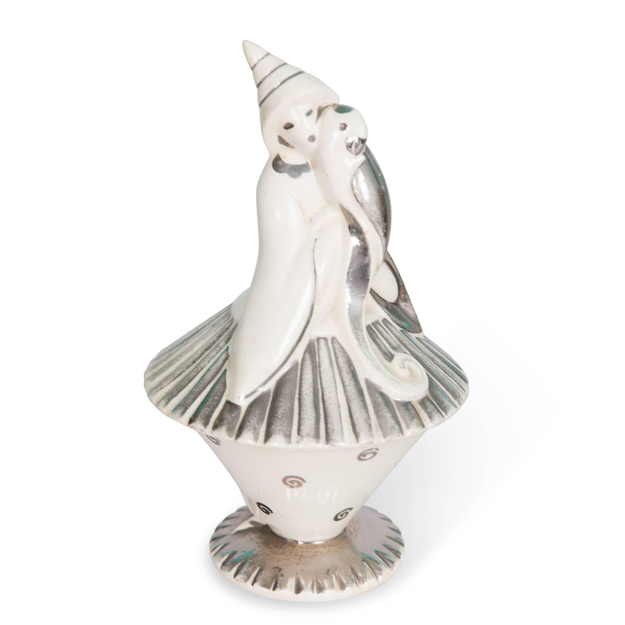 White porcelain lidded bowl, with silver accents, in the form of a harlequin type figure holding a dove by Primavera, France, 1930s. Stamped signature to underside. Measures: Height 8 1/2 in, largest diameter 5 in. 