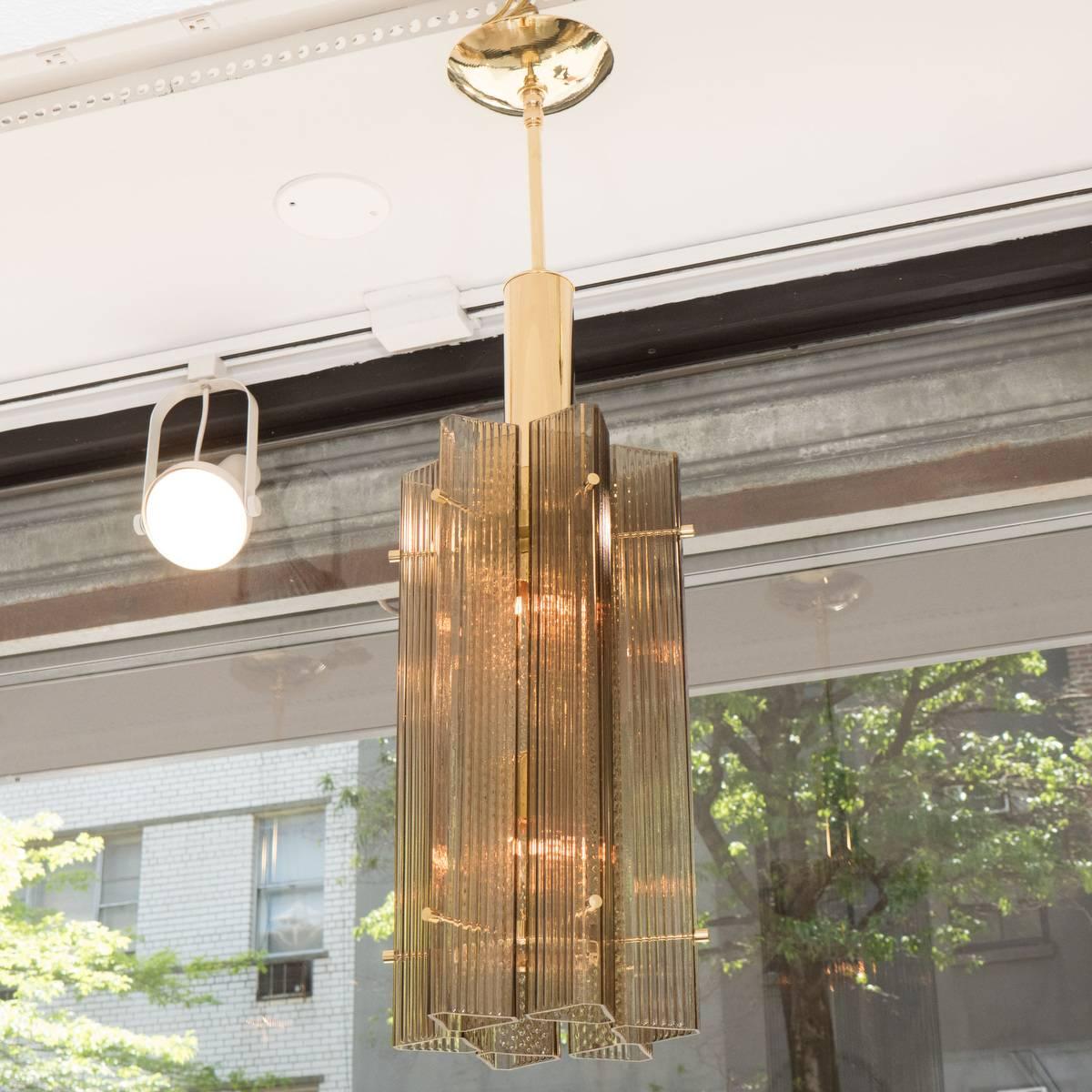 Brass pendant ceiling fixtures composed of clustered smoked and fluted glass tube elements.