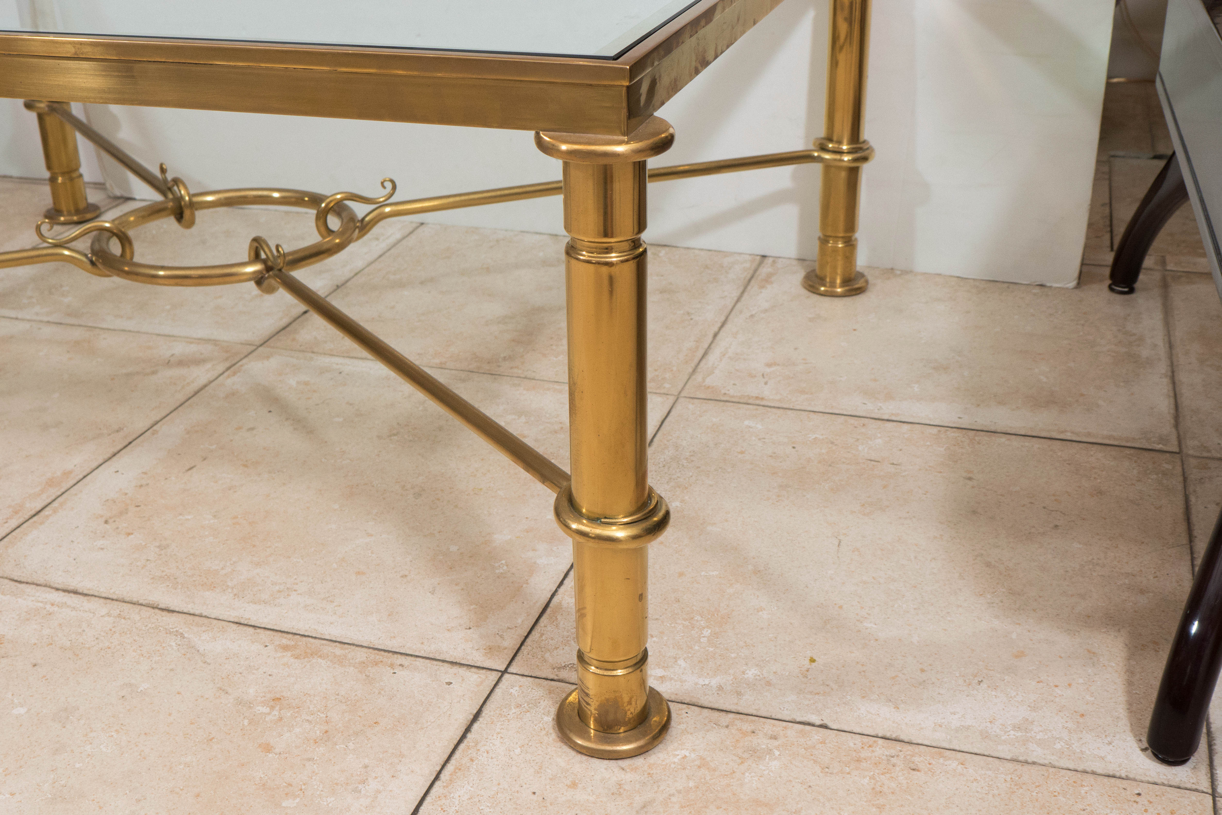 Rectangular brass coffee table with glass top and brass cross bar design.
