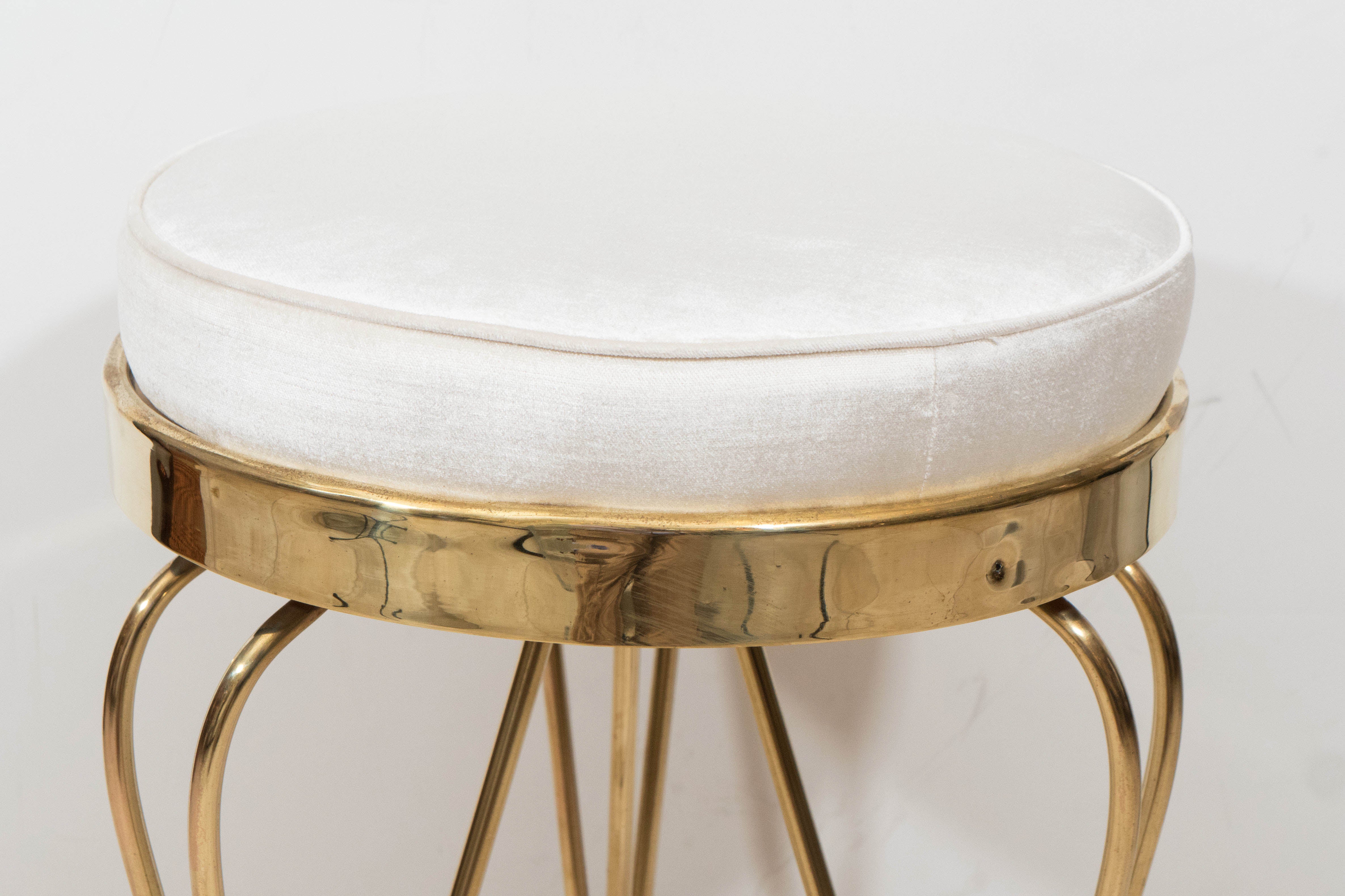 Pair of petite round upholstered stools with curvilinear brass legs.