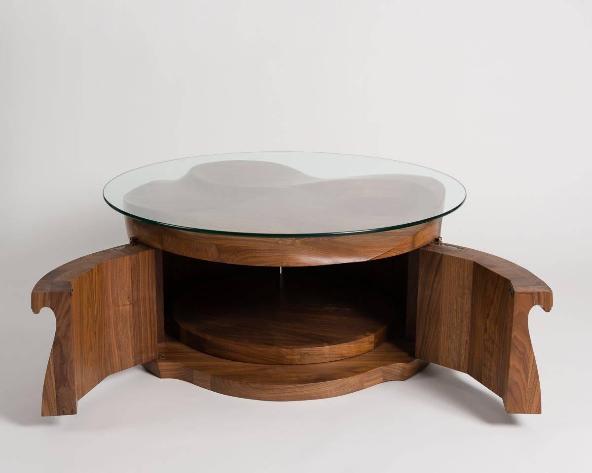 This sculptural table is carved into a flowing arrangement from solid, three and a half inch walnut, and features double doors that open up onto an interior cabinet with a revolving floor.