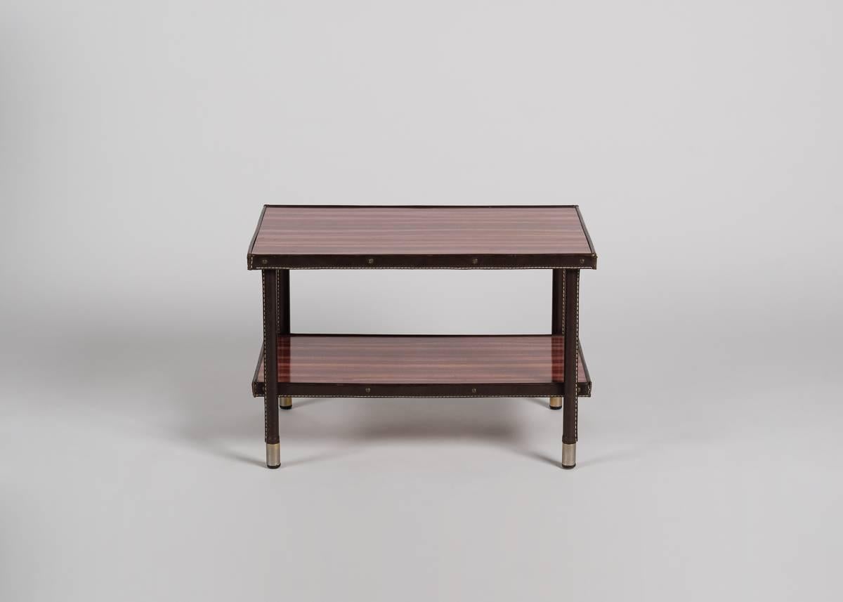 A two tiered rectangular side table with a laminated top, leatherette clad legs and brass sabots.