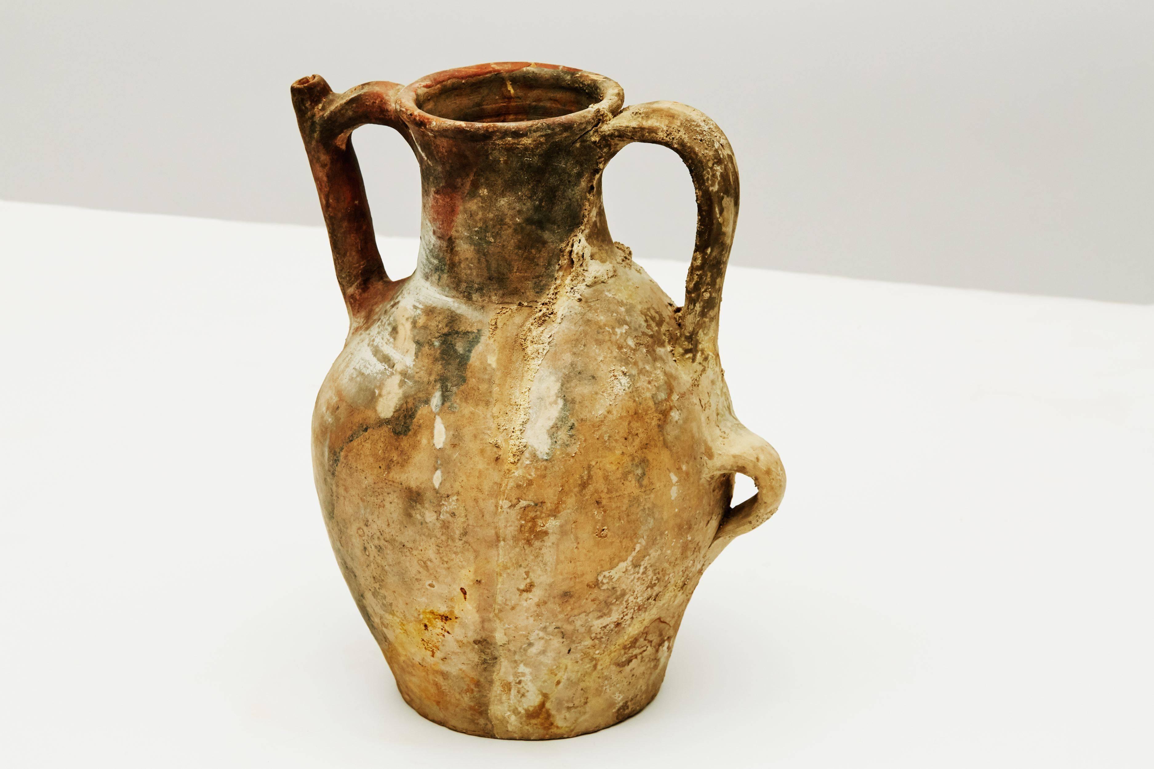 A ceramic jug hailing from Central Europe, and created in the mid-19th century, this piece, which was once held in famed designer Liz Claiborne's private collection, is glazed in earth tones, constructed with two handles, and possesses a long,