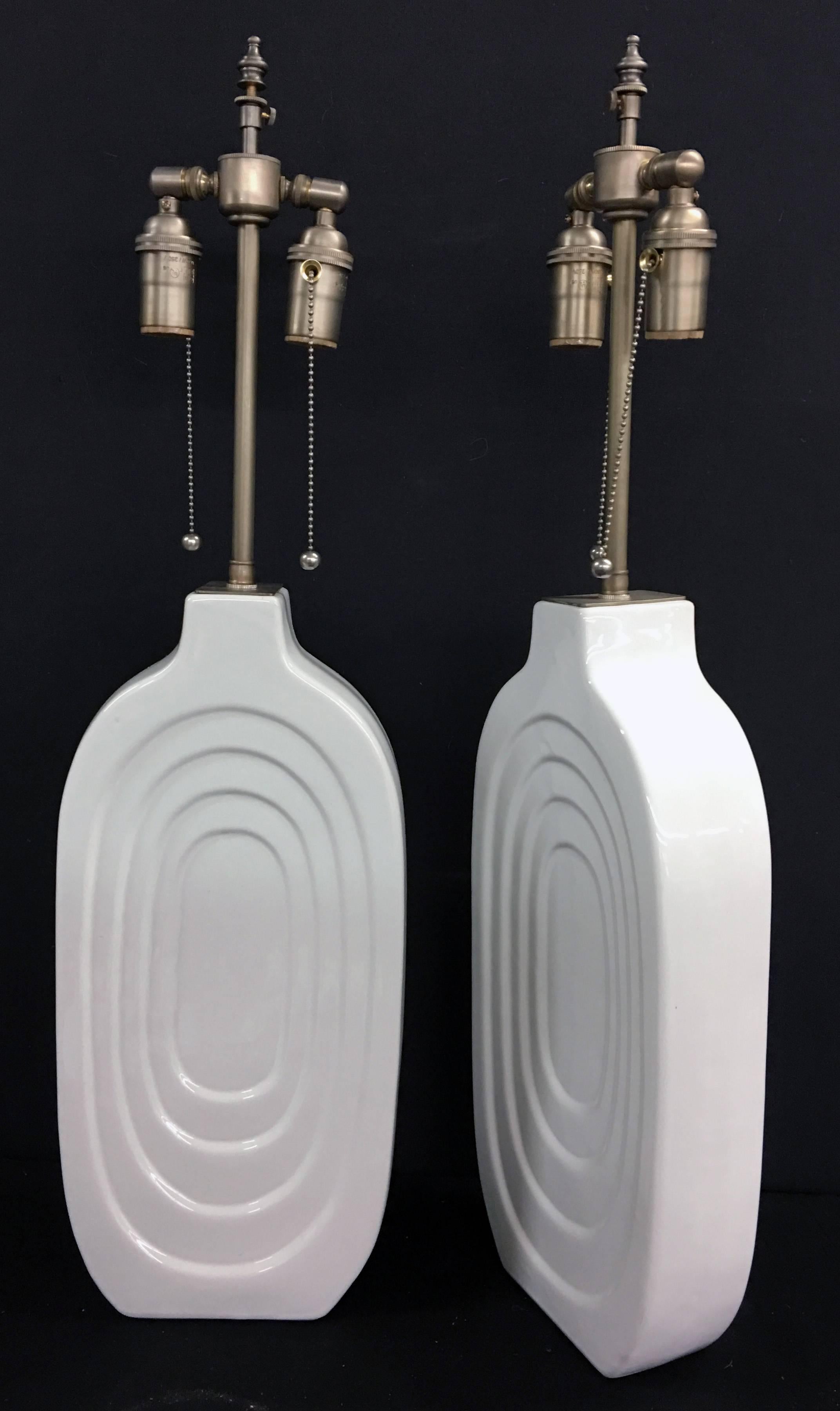 Unique pair of White ceramic, glazed mid-century vessels with lamp application. The lamps are newly wired. The hardware is brushed nickel with dual socket, individually controlled pulls. The vessel height is 171/2", the shade post height is 28