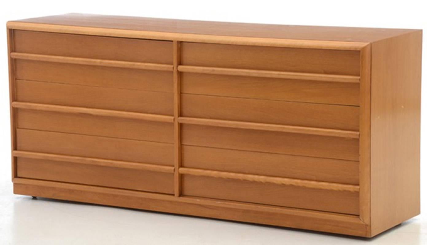 A Mid-Century Modern dresser by British Modernist designer T.H. Robsjohn-Gibbings, in veneer with a light finish. It has six drawers with finger grip pulls, with some drawers being partitioned into segments, and with a sliding tray to the top right