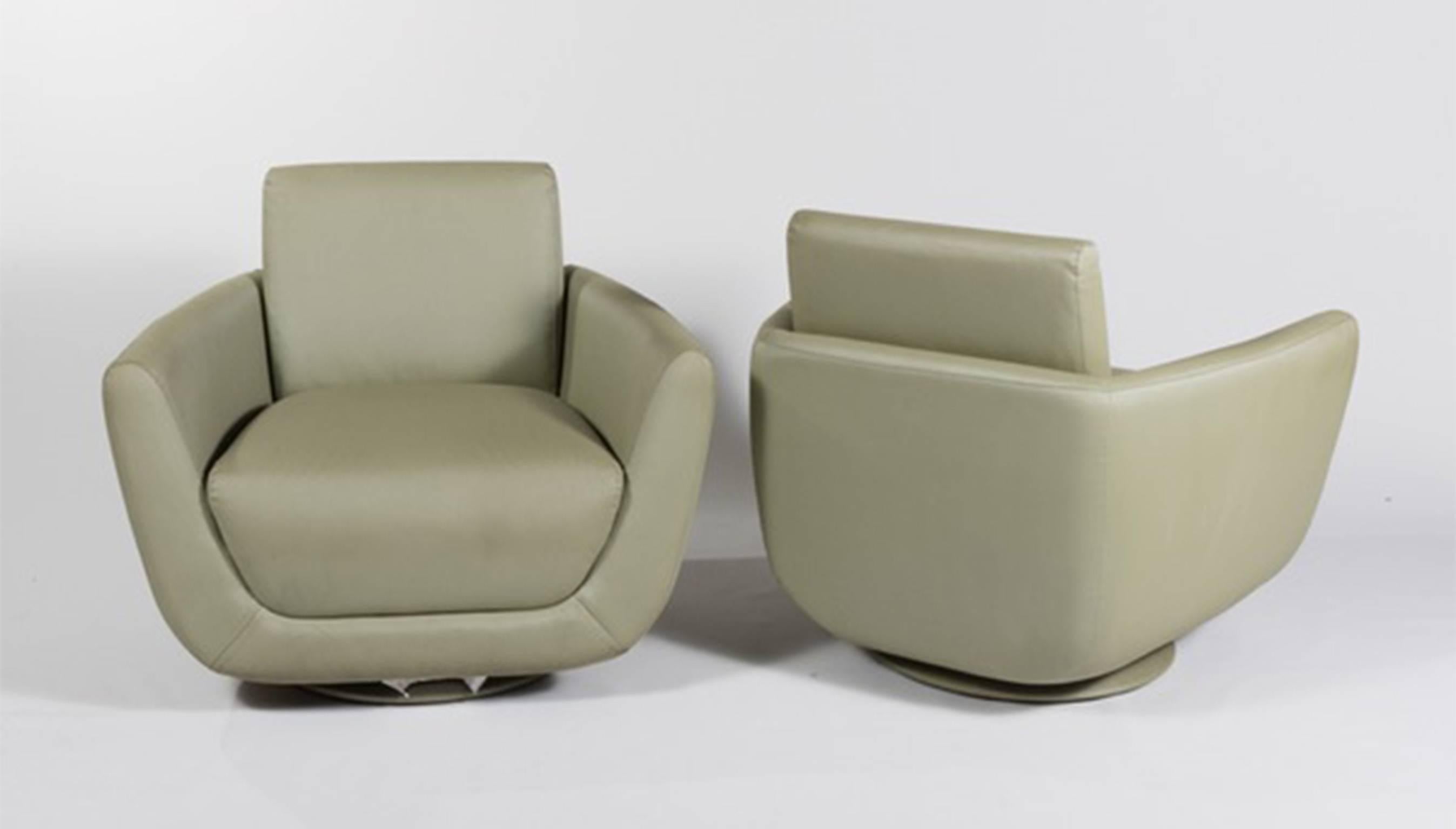 A pair of Mid-Century Modern swivel armchairs. The chairs feature a green leather-like upholstery, a removable seat cushion and a circular swivel base.