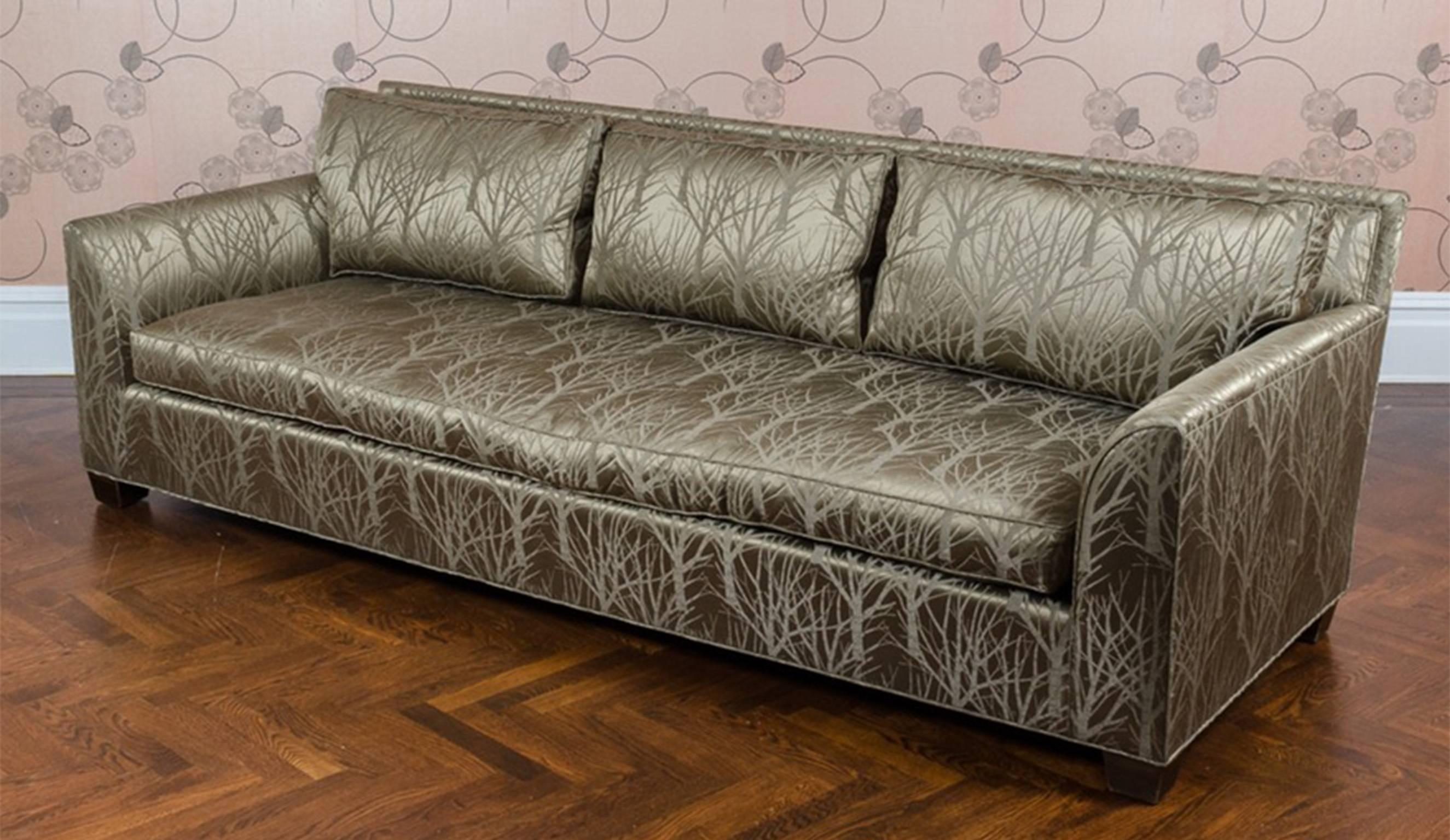 A gray metallic tree Silhouette upholstered sofa. This contemporary style sofa features a metallic upholstery with a pattern of tree silhouettes. It has three back pillow and one seat cushion. The arms curve inward toward the seat. The sofa stands