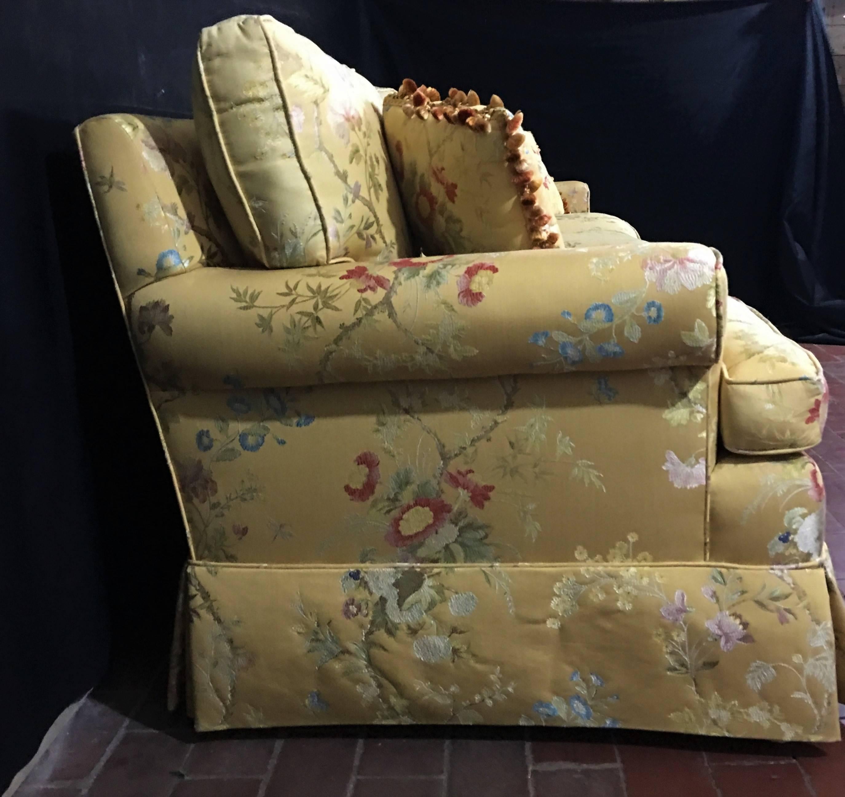 Large two-piece sectional sofa in pale yellow brocade with colorful floral pattern. The seating composition is foam core/down wrap. The back cushions are all feather as are the pair of matching throw pillows with colored fringe trim to match the