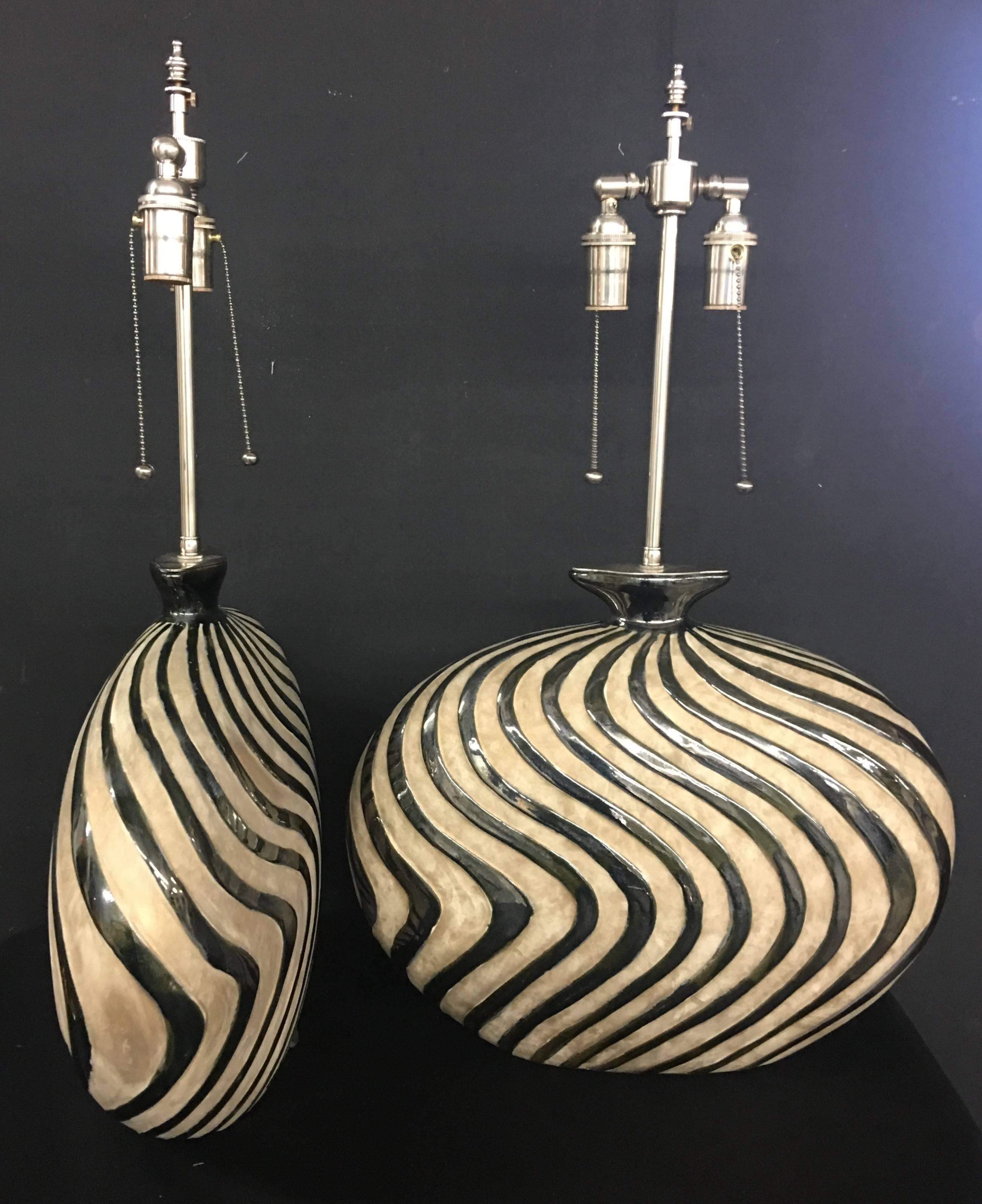 Unusual pair of whimsical ceramic vessels with lamp application. The vessels are in a mottled cream background with raised silver glazed waves. The hardware is polished nickel. The vessels are 15.5