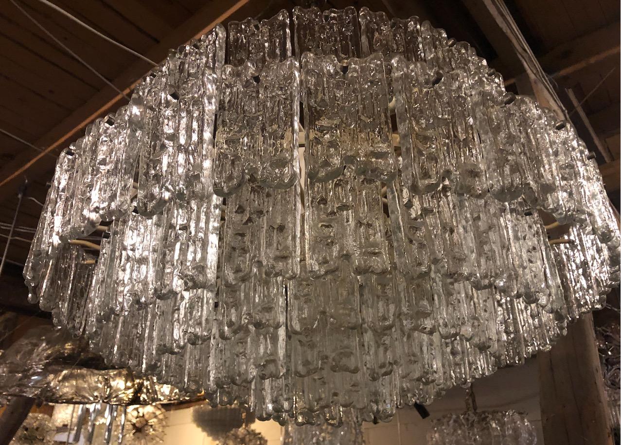 A large chandelier consisting of multiple tiers of textured glass hung on a metal frame with brass hardware, rod and canopy by J. T. Kalmar.

Austrian, Circa 1960's