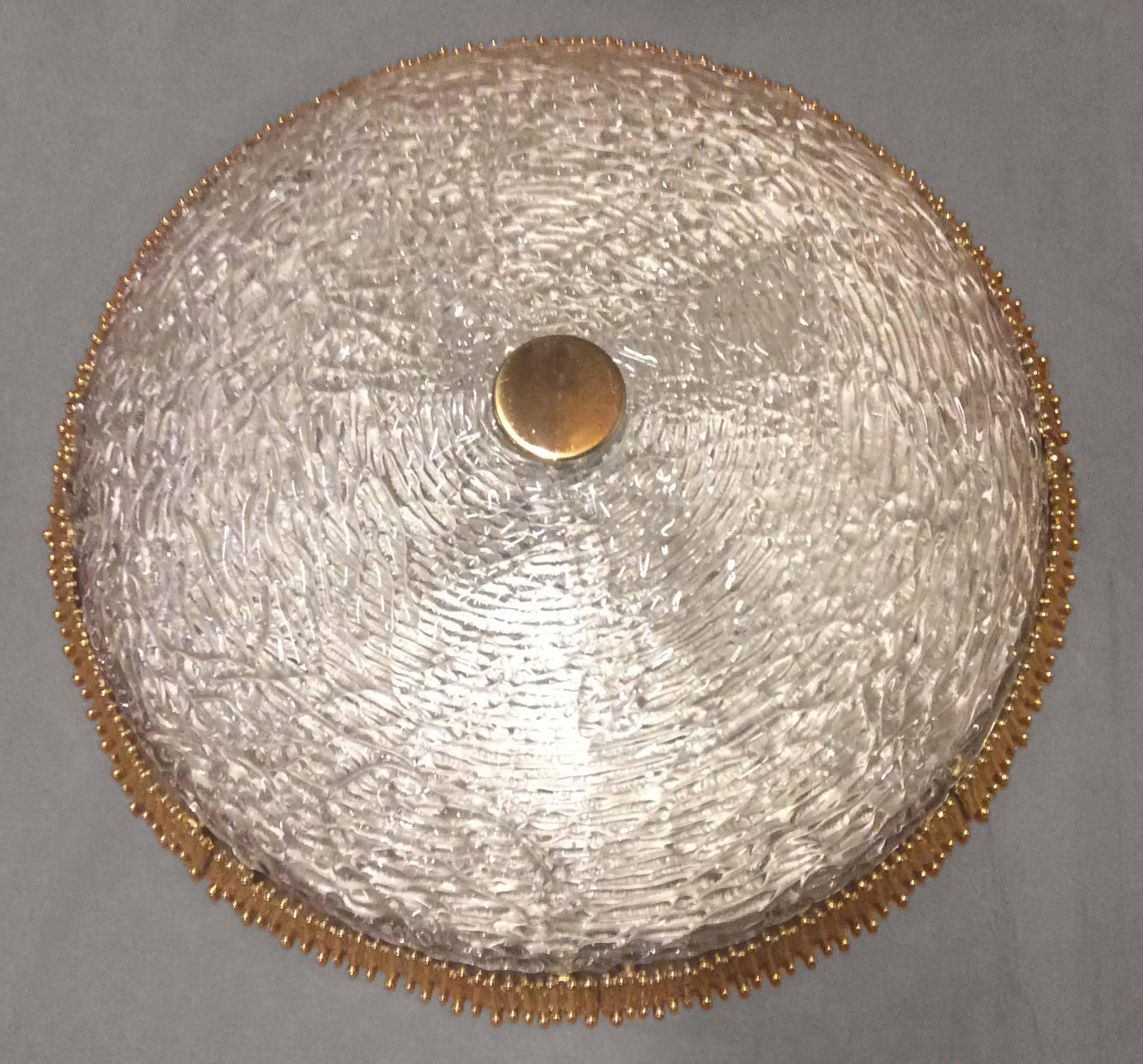 A flush mount textured clear glass fixture with circular textural brass detail by Hillebrand or Kaiser.

Circa 1960's

Two (2) Are Available.