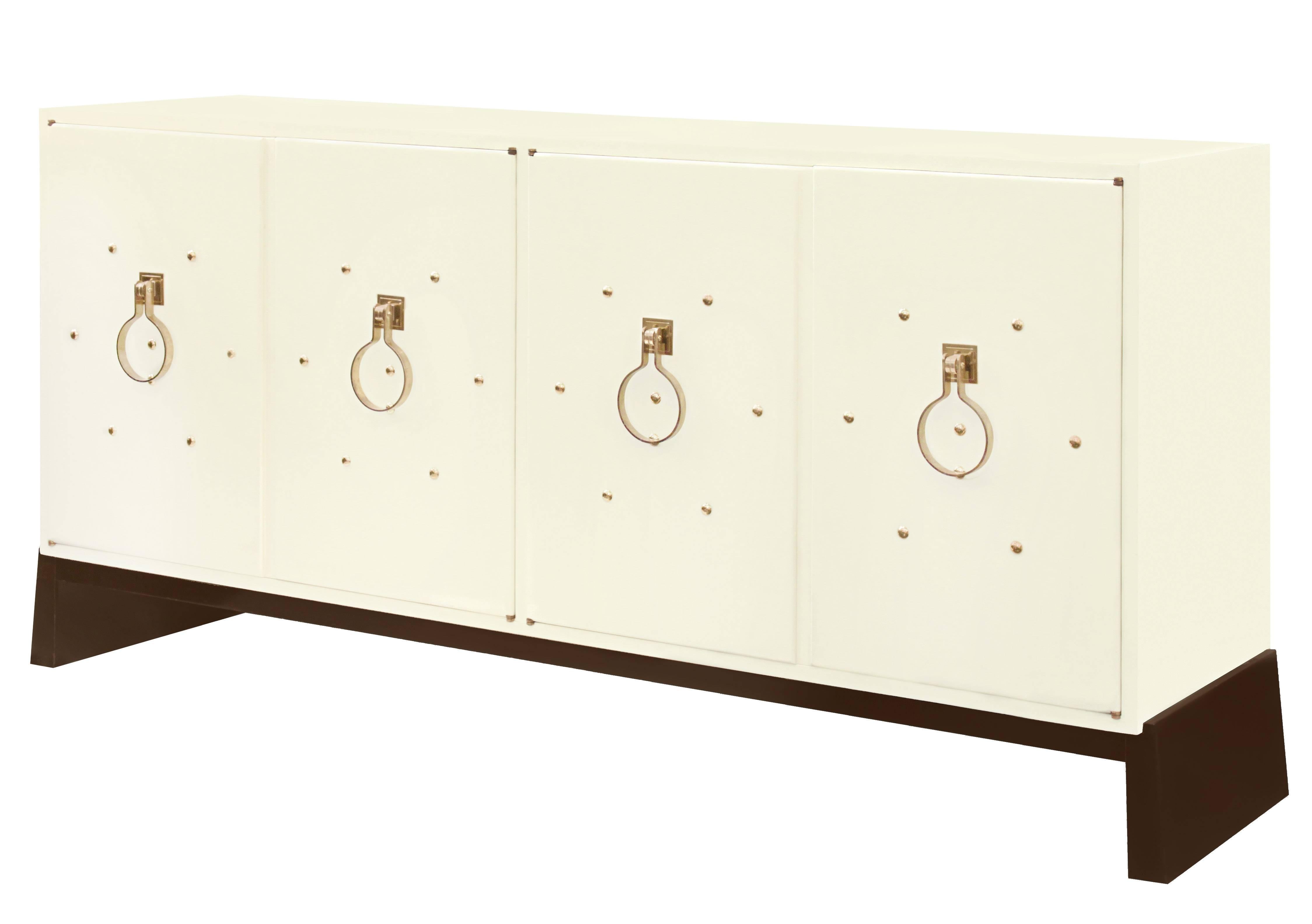 Exceptional four-door credenza in ivory lacquer with brass studs and iconic pulls on a dark mahogany base by Tommi Parzinger for Parzinger Originals, American 1950s (signed “Parzinger Originals” in drawer). This is a beautiful example of Parzinger's