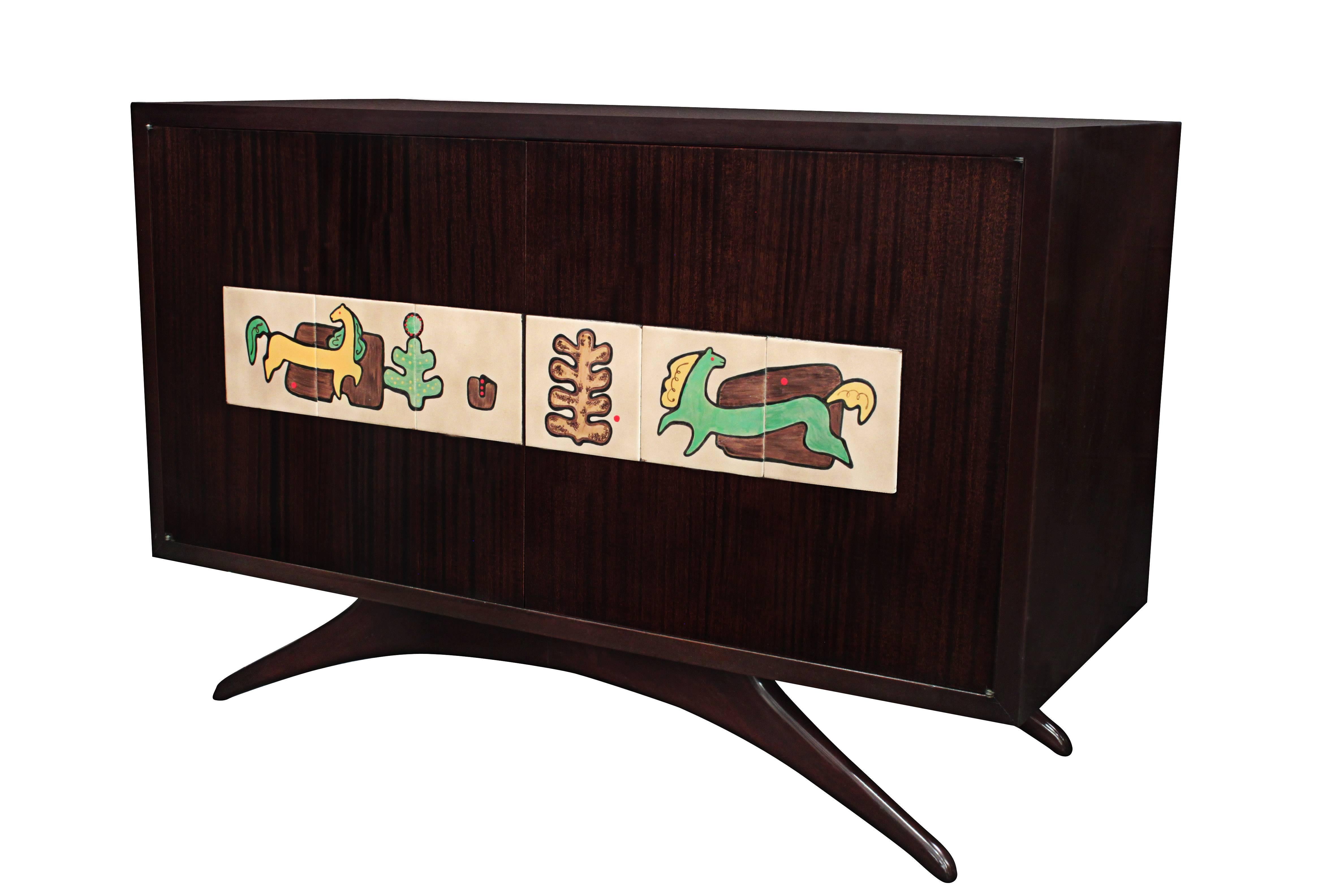 Rare and early cabinet in mahogany with iconic splayed legs and hand painted ceramic tiles by Alexandra Kasuba on doors by Vladimir Kagan, American, 1950s. Alexander Kasuba was a Russian artist who often collaborated with Kagan. The interior is clad