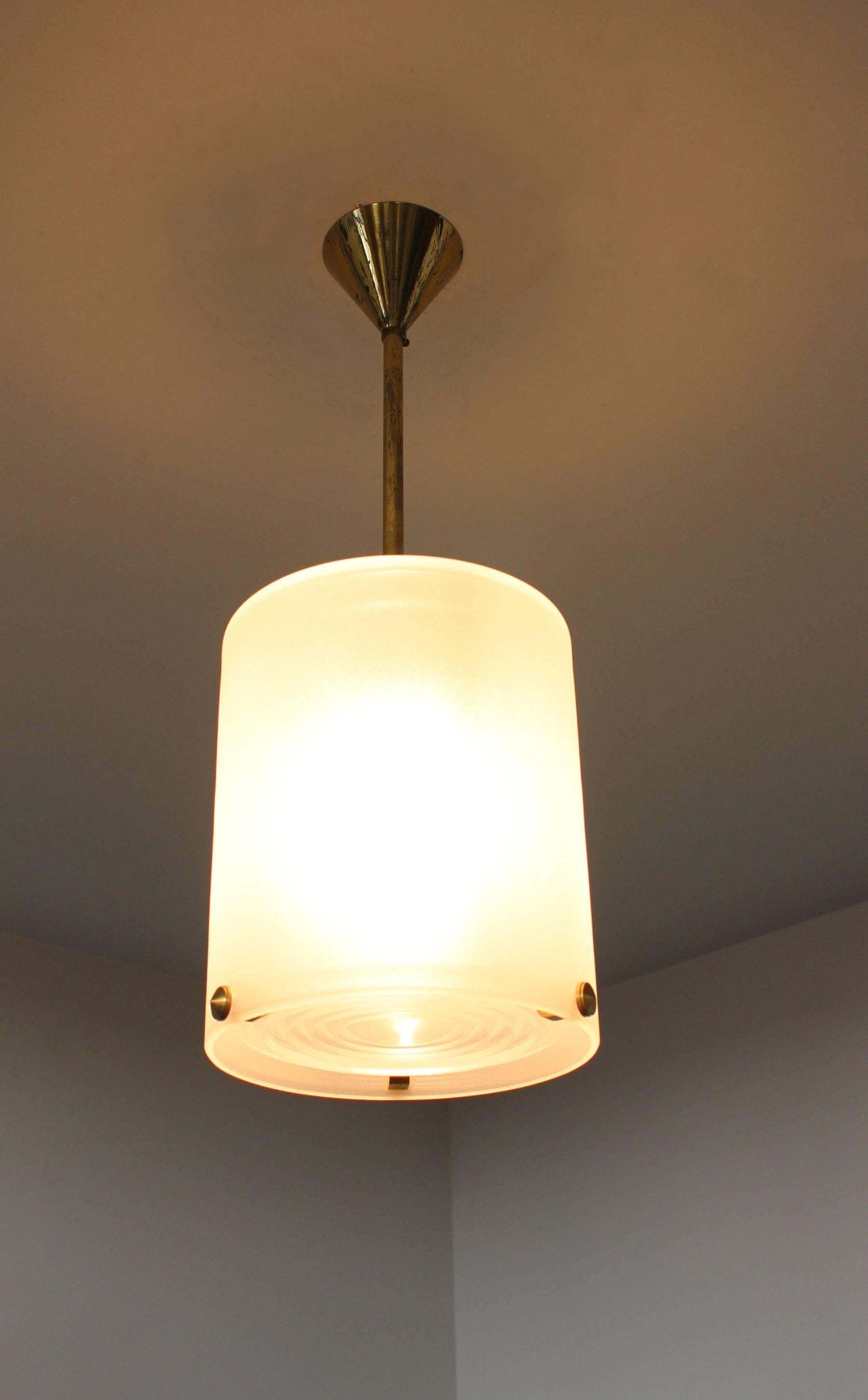 A fine French Art Deco pendants by Jean Perzel with a frosted glass cylinder shade and three bronze studs that support a prismatic glass lens, the rod and canopy are bronze as well. 
