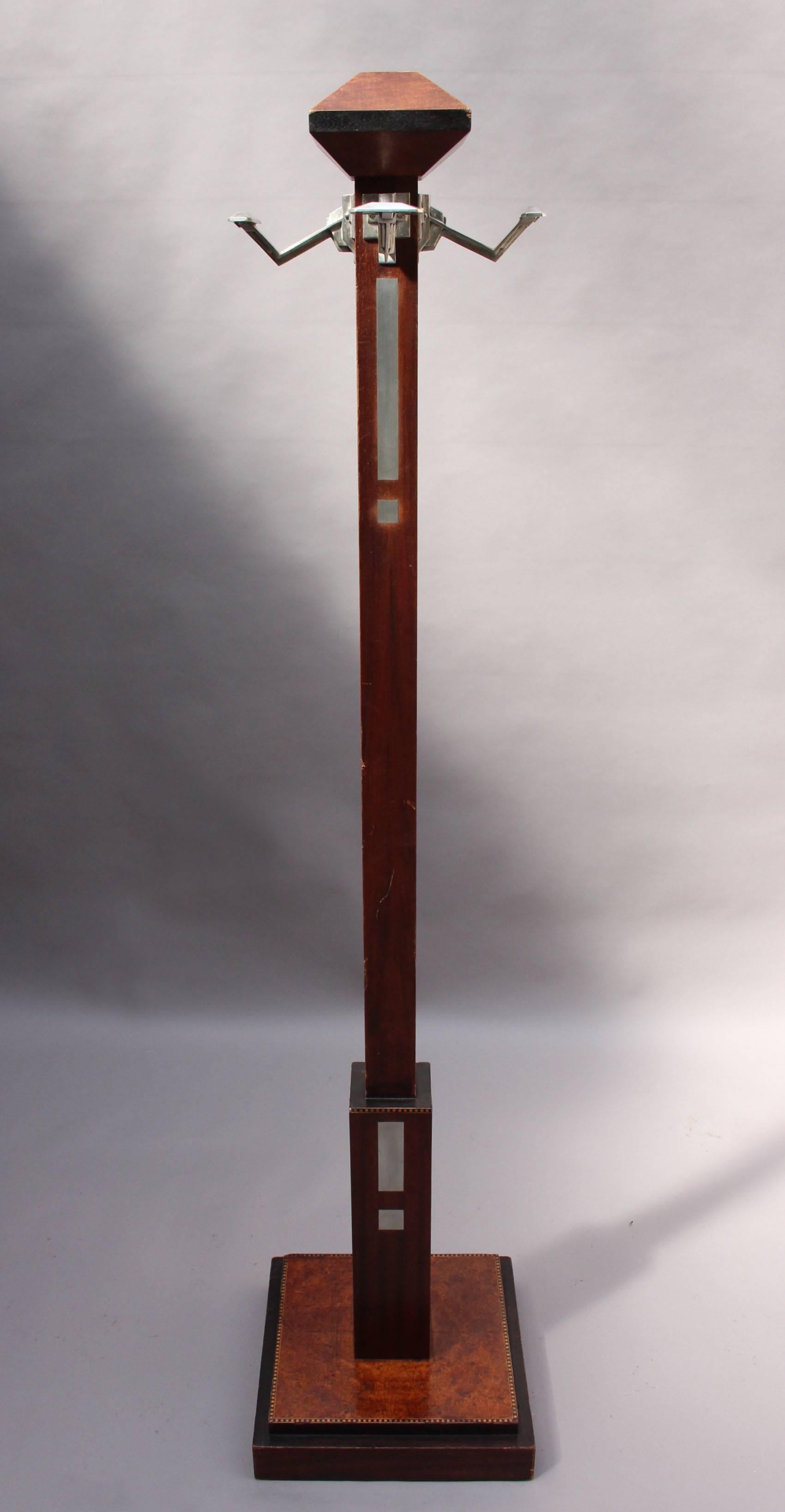 A fine 1900's coat rack with a burled wood and marquetry base, a mahogany with marquetry and metal inlay stem that holds four metal coat or hat hooks, and a trapezoidal wood tip.