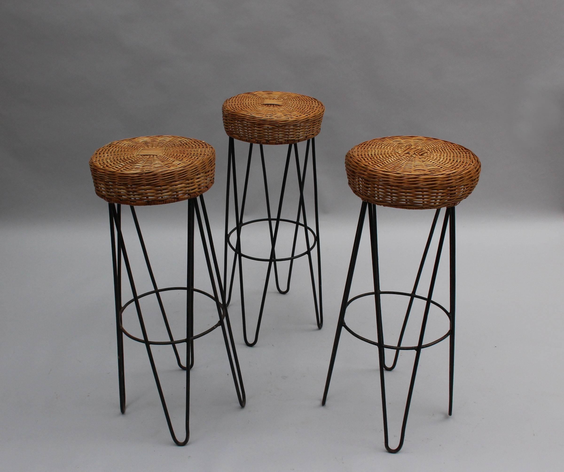 Three French Mid-Century bar stools with a curved tubular black metal base and a round rattan seat.

Price is per stool.