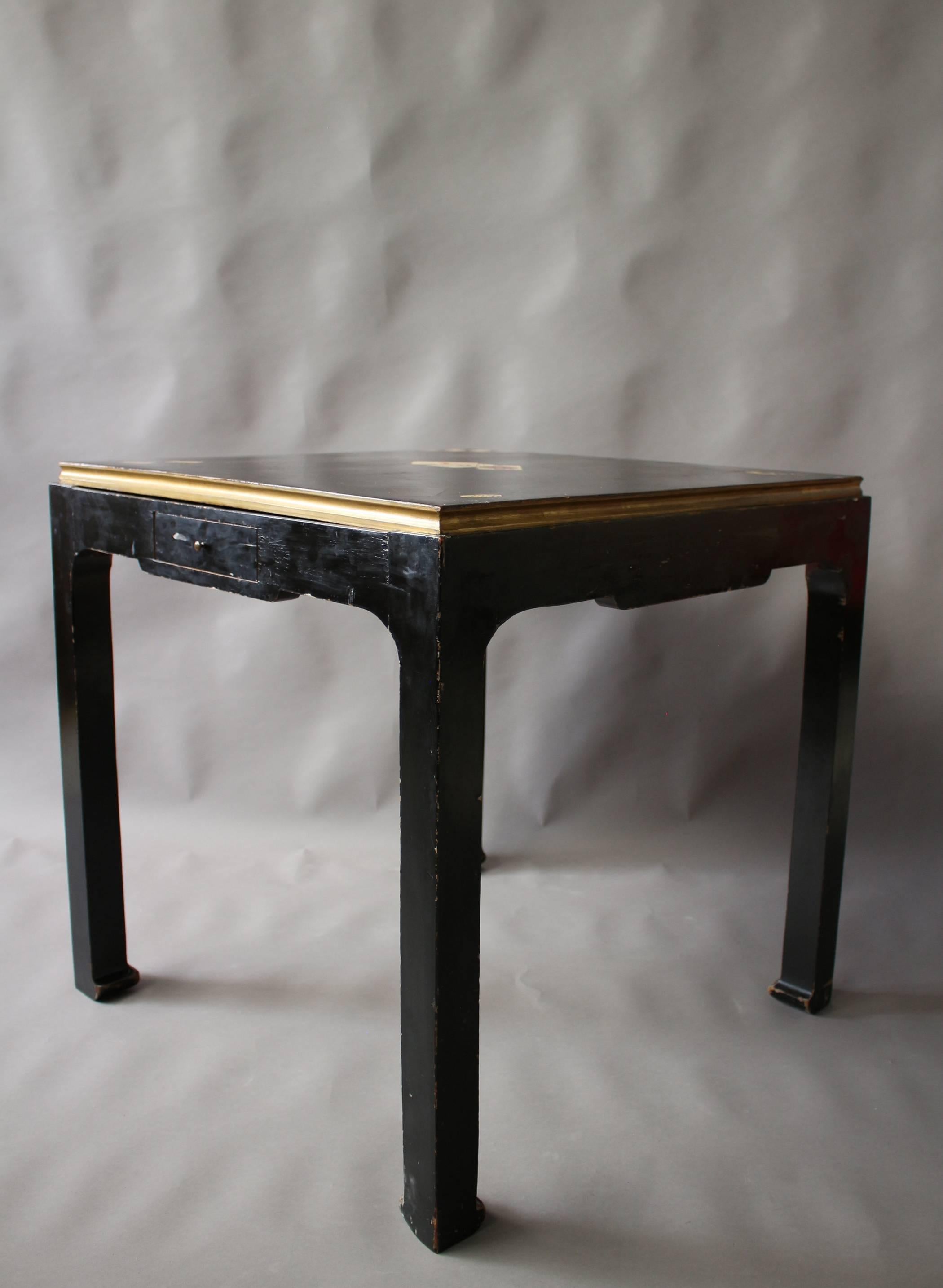 A French Art Deco black lacquered game table with a reversible top, one side with games theme inlay, the other side felt covered - four Asian style legs and one drawer.