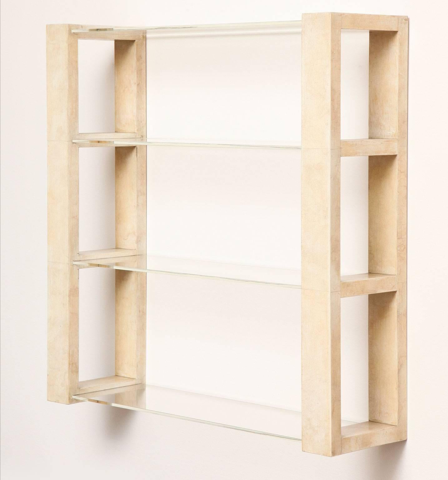Wall-hanging bookcase in wood with crackle lacquer finish and four glass shelves. Manufactured by Quigley & Company.