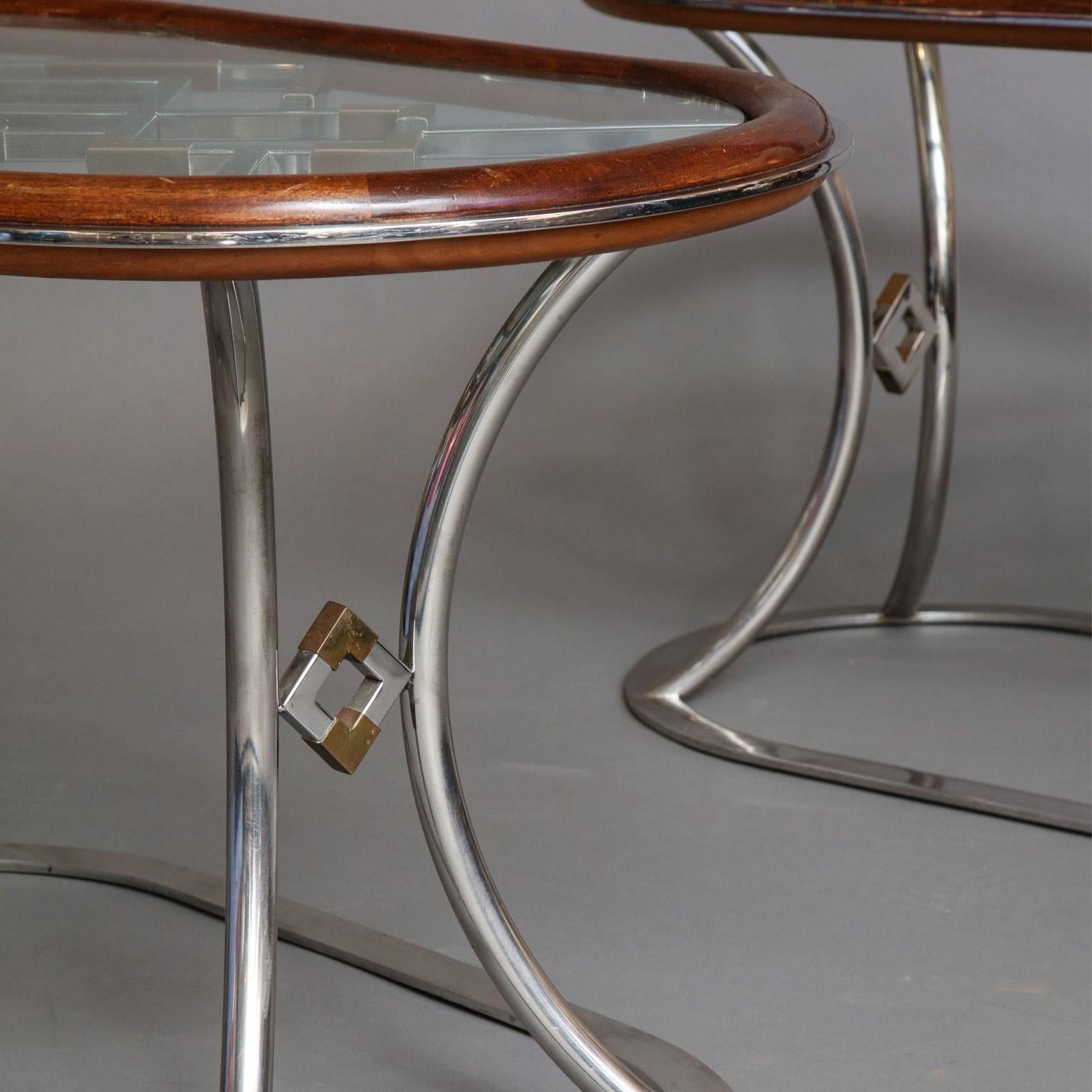 Alain Delon for Maison Jansen
Mixed metal oval side tables in chromed steel with patinated bronze details. Glass top surrounded by bull nose mahogany trim resting on geometric lovers knot base.
French, circa 1970.
 