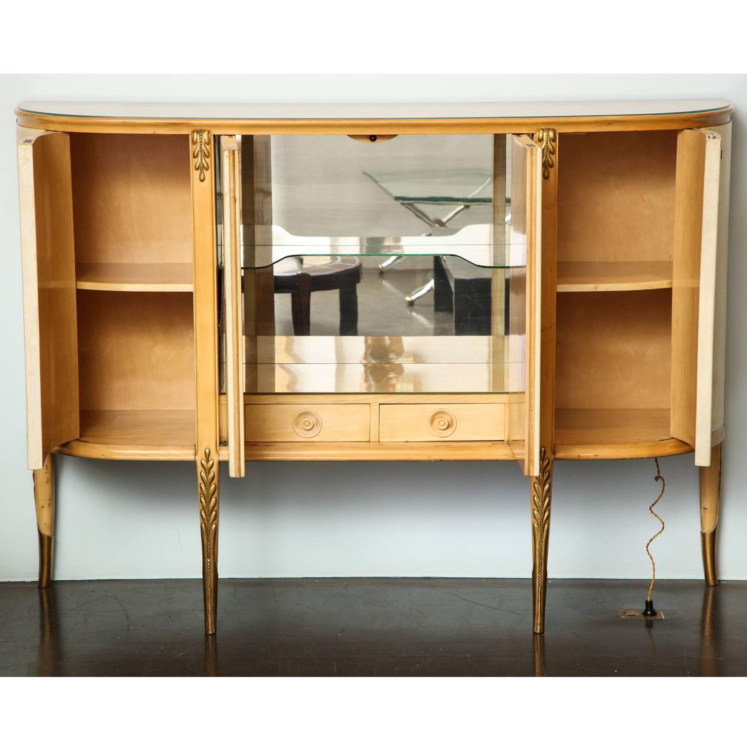Giovanni Gariboldi (1908-1971)
Illuminated bar cabinet in sycamore, pearwood and carved
giltwood, with fruitwood inlaid parchment doors. The central compartment opening to reveal one glass shelf and two sycamore drawers the sides open to reveal one