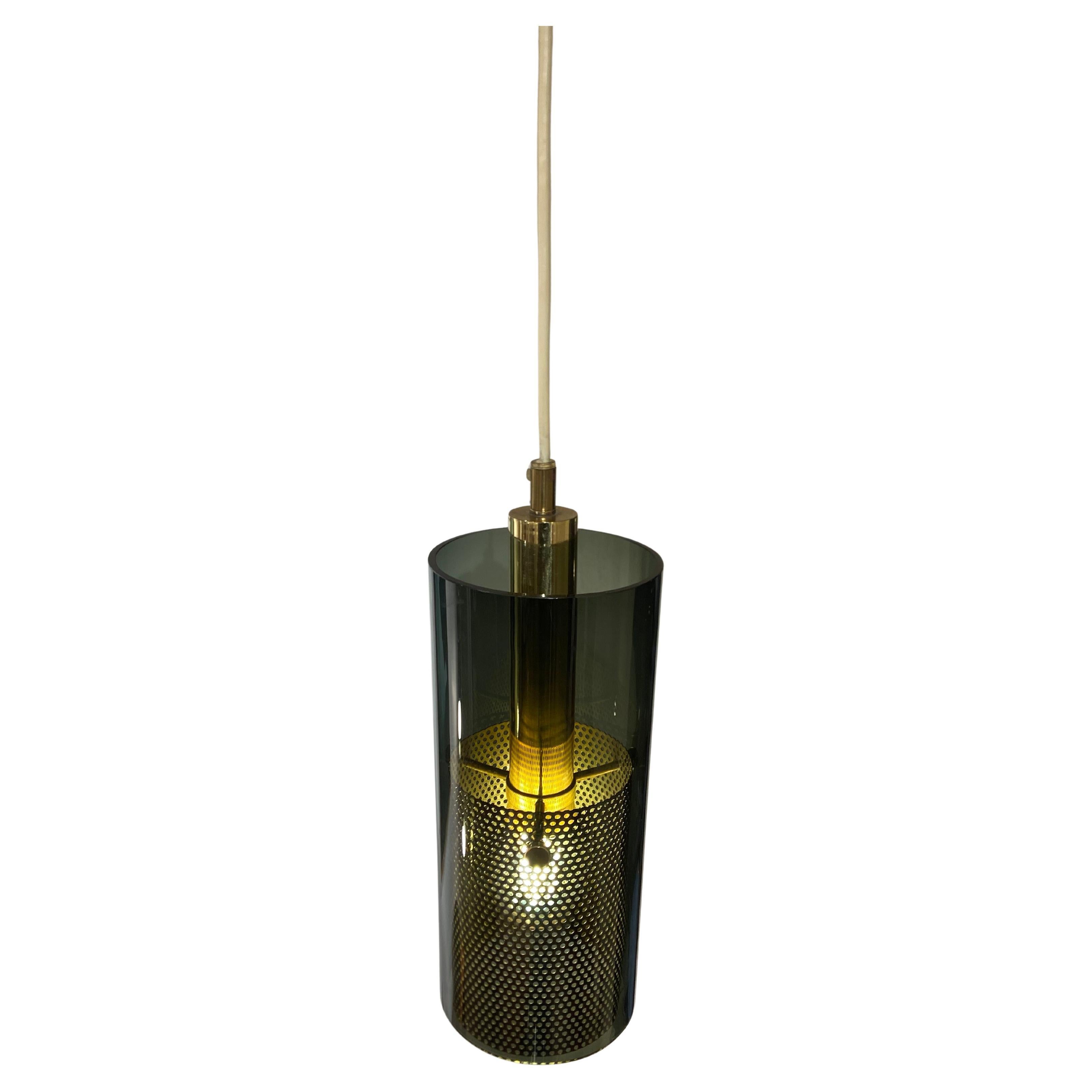 Rara lampada a sospensione di Hans-Agne Jakobsson composta da un paralume cilindrico in vetro fumé con un diffusore interno perforato, fissato con tre viti e una base sottile, tutto in ottone. L'ingegnoso assemblaggio di materiali e l'estetica