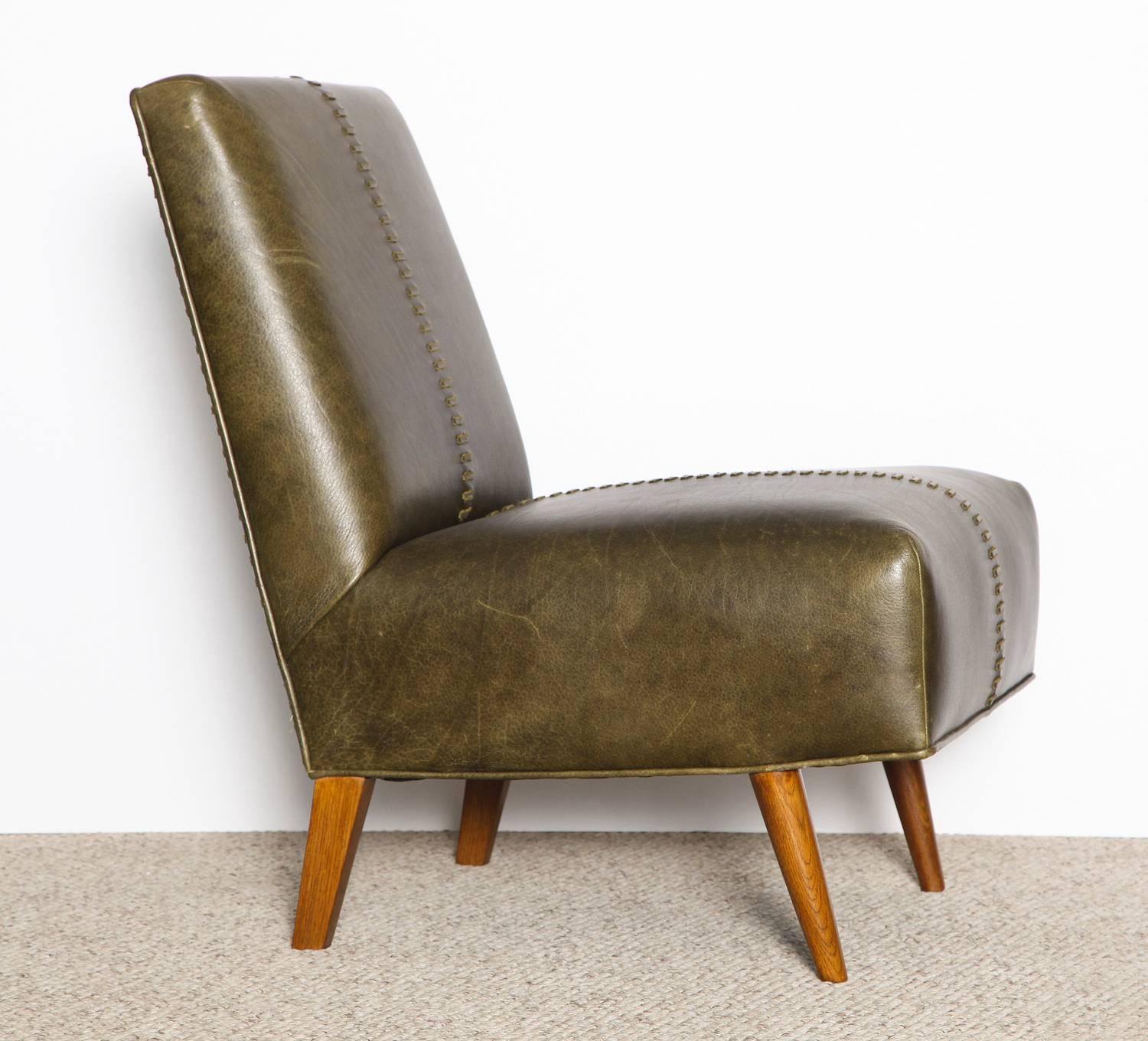 Pair of armless lounge chairs by Paul Laszlo.   Olive green leather upholstery with great stitching details. Tappering legs of dark-stained oak. These chairs were custom designed for the John Hudspeth Estate in Prineville, OR.